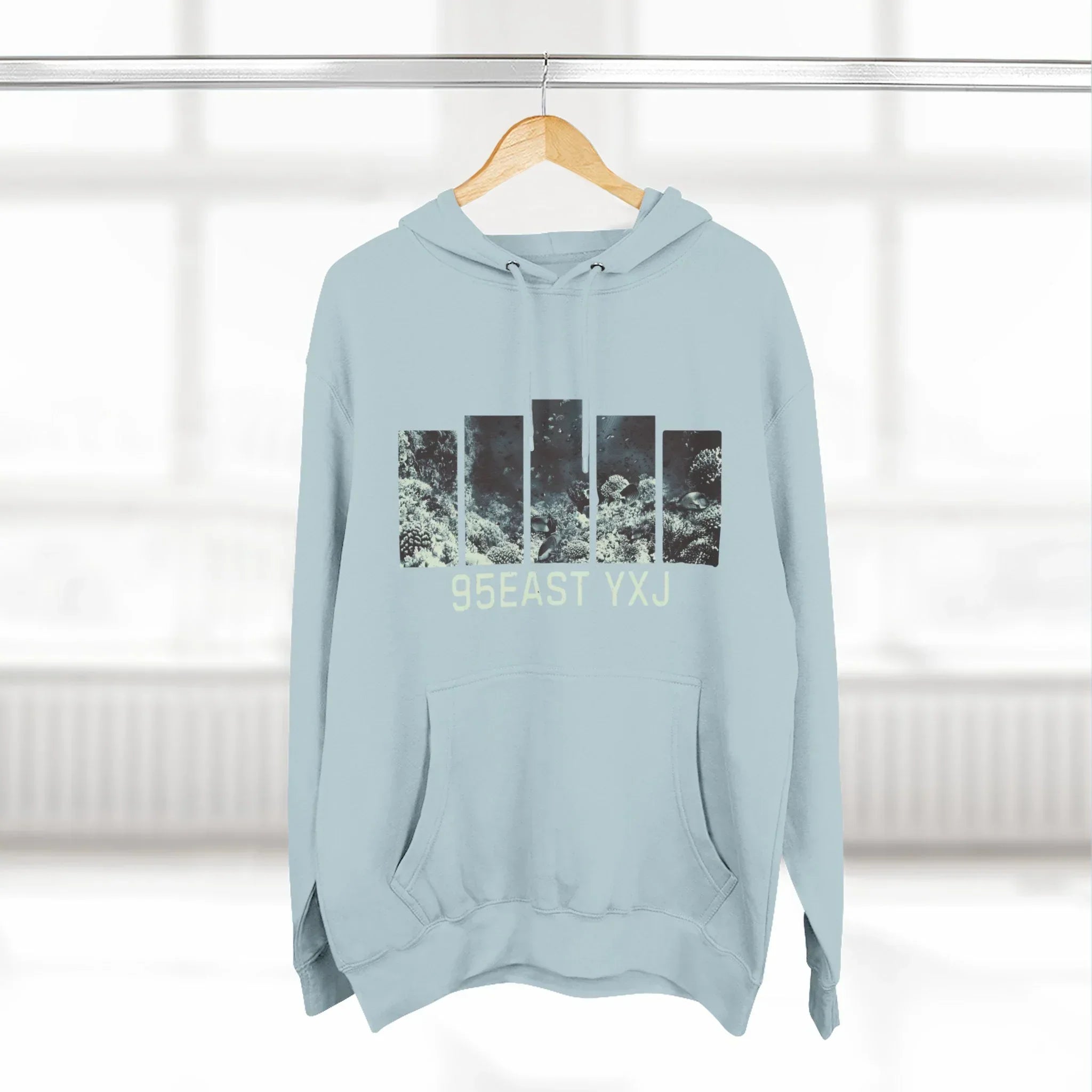 Light blue hoodie with abstract black graphic and '95EAST YXJ' text, hanging indoors