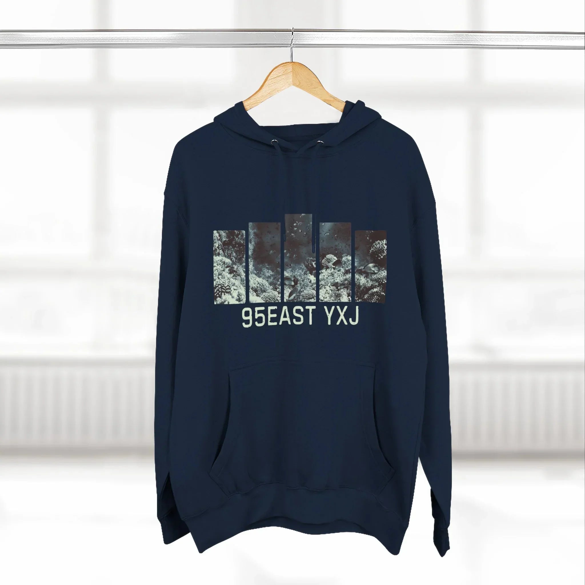 Navy blue hoodie with abstract graphic bars and 95EAST YXJ text, hanging on wooden hanger