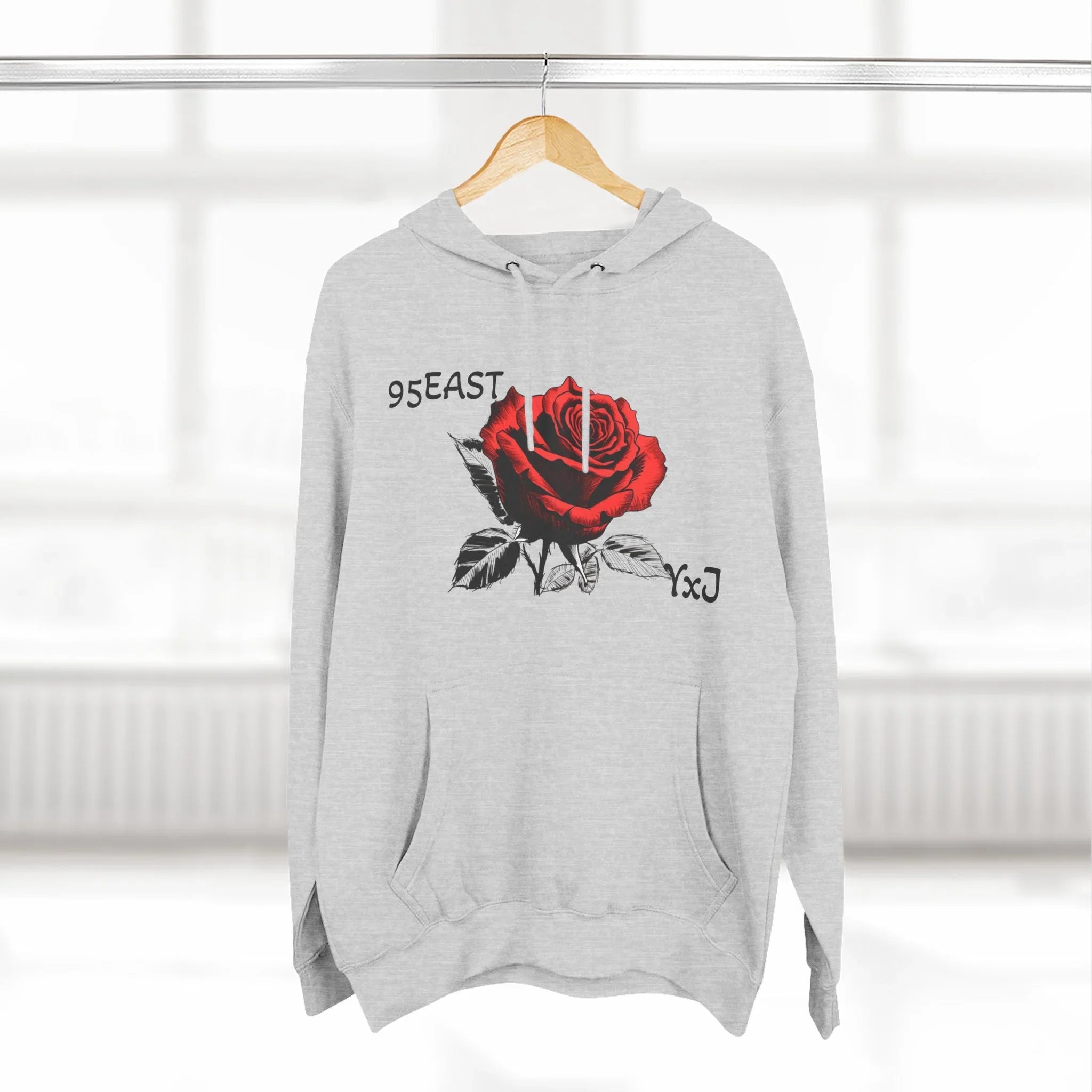 Gray hoodie with red rose graphic and 95EAST YxJ text, hanging on wooden hanger