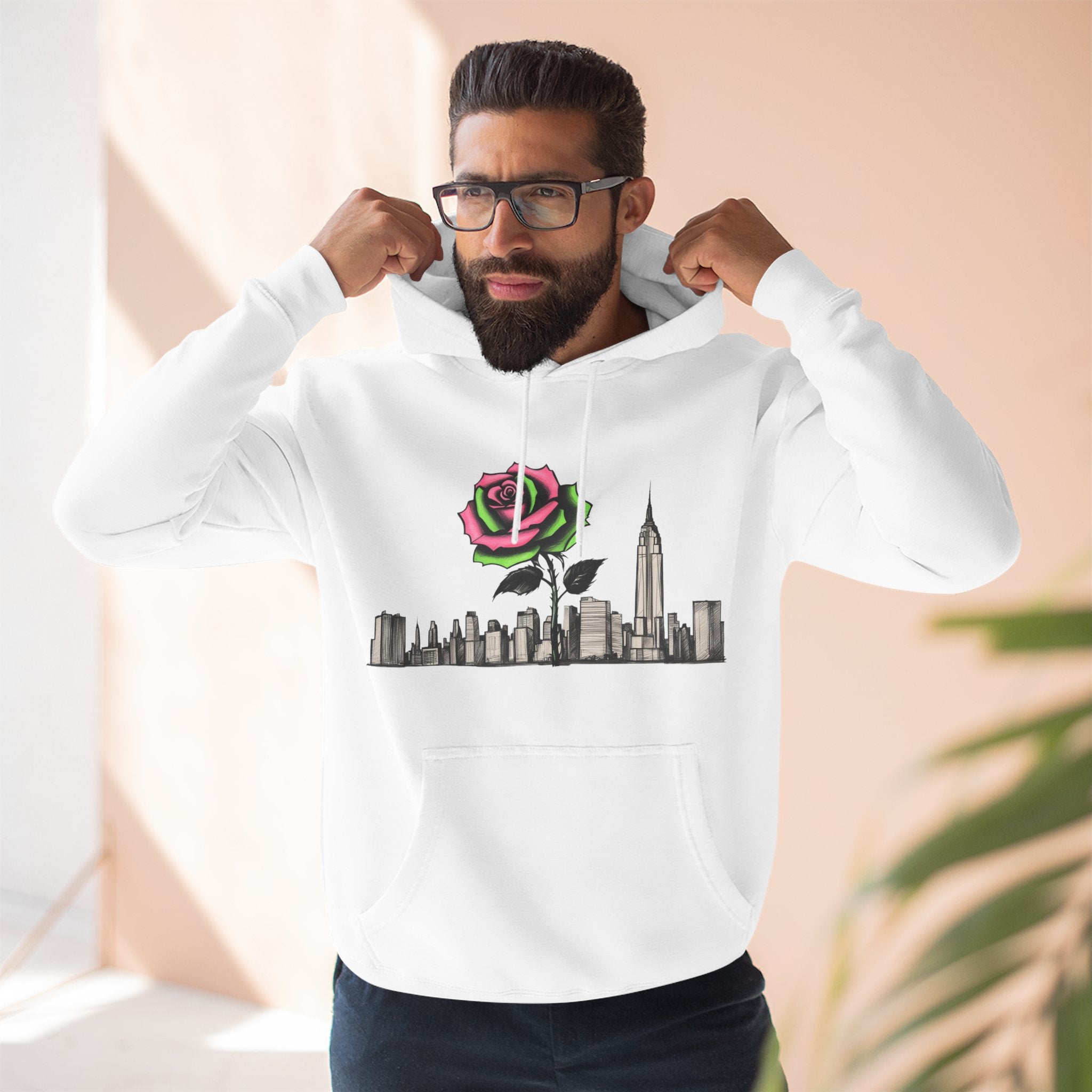 White hoodie with rose graphic over city skyline, worn by man adjusting hood