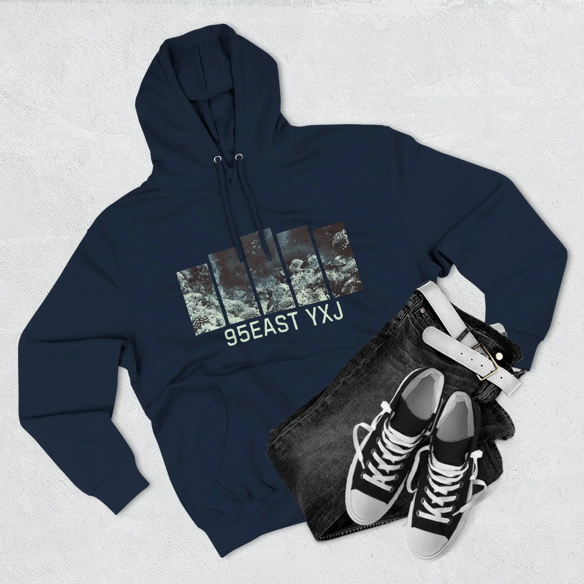 Navy blue hoodie with graphic print and 95EAST YXJ text, paired with black jeans, belt, and sneakers