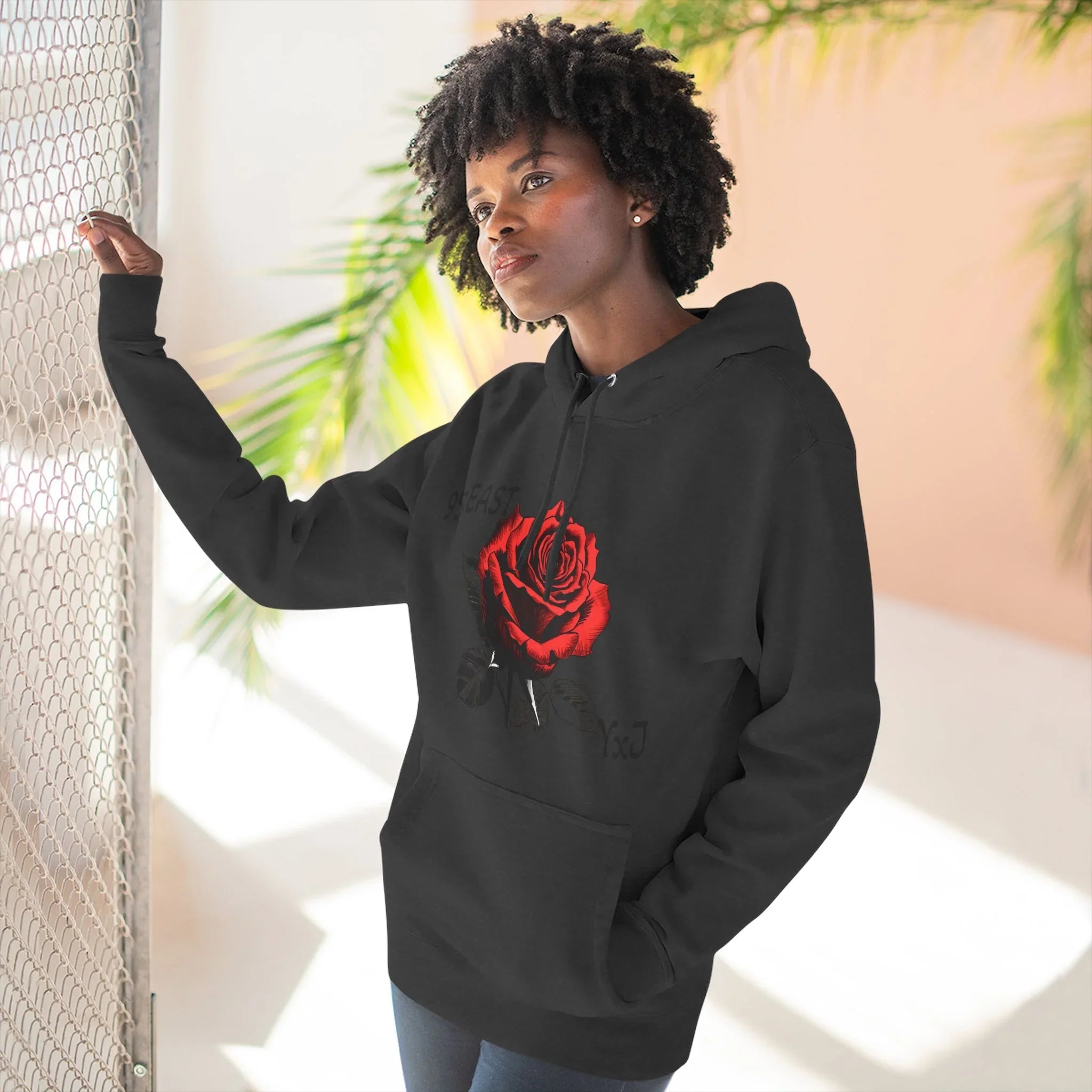 Black hoodie with red rose graphic and barcode sleeve detail, worn by woman near mesh fence