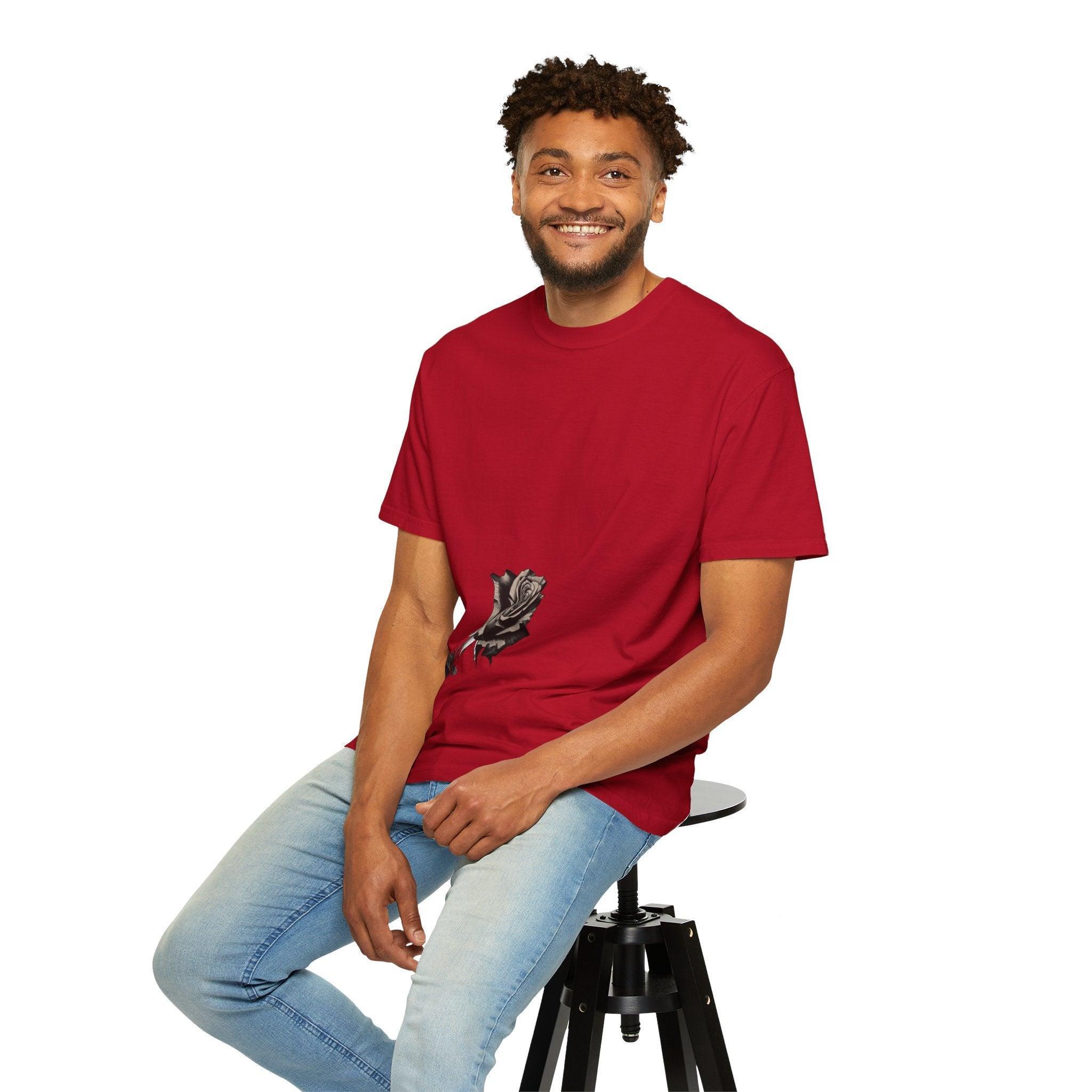 Man wearing red graphic tee with black rose design, paired with light jeans, seated on stool