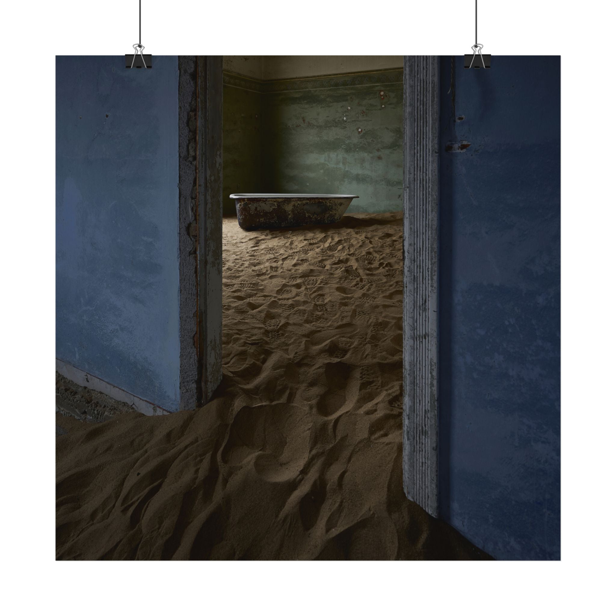Abandoned room with sand-filled floor, rusted bathtub, and peeling blue walls, evoking decay and desertion.