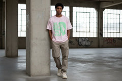 Man wearing pink graphic tee with green text, standing in urban loft with graffiti