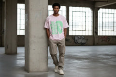 Man wearing pink graphic tee with green text, standing in urban loft with graffiti