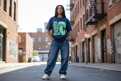 Woman wearing navy tee with green graphic text 'We Created What You Wear' on urban street