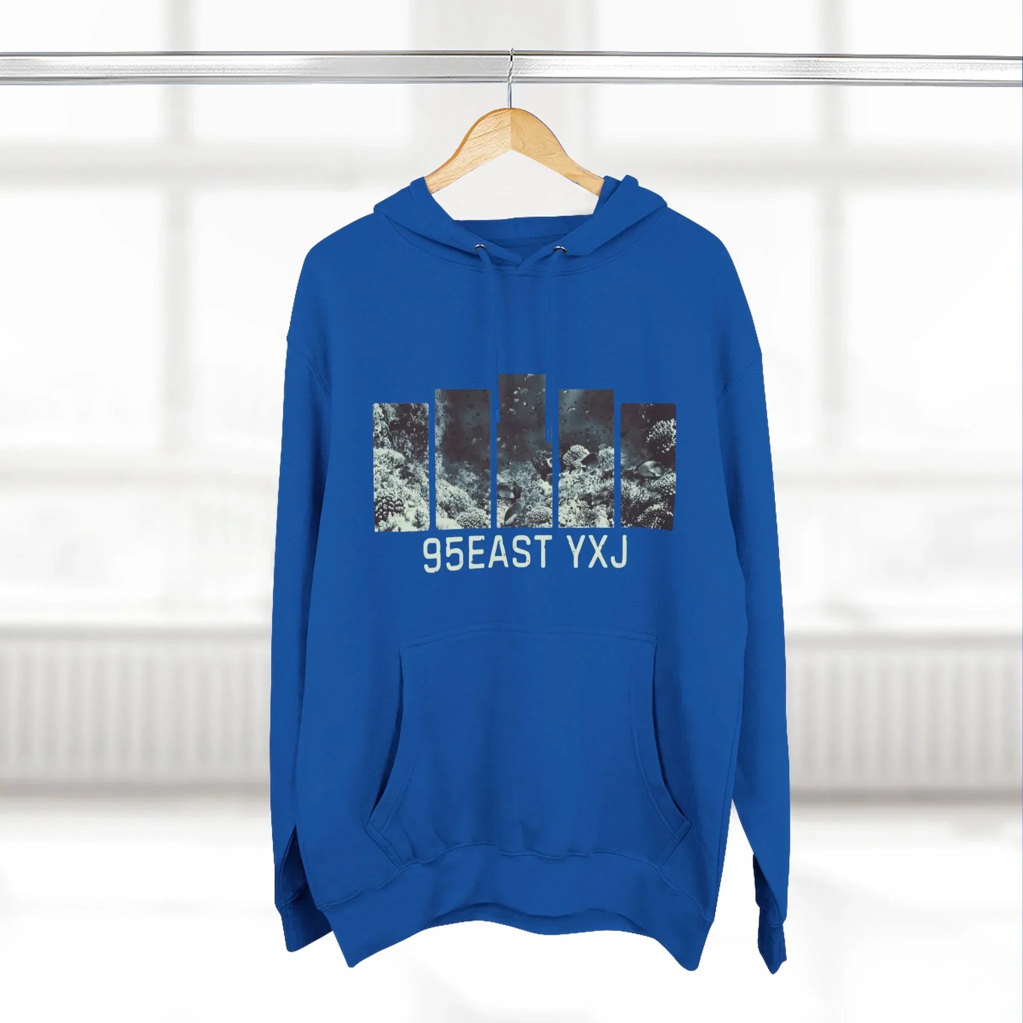 Blue hoodie with abstract vertical graphic and 95EAST YXJ text, hanging indoors