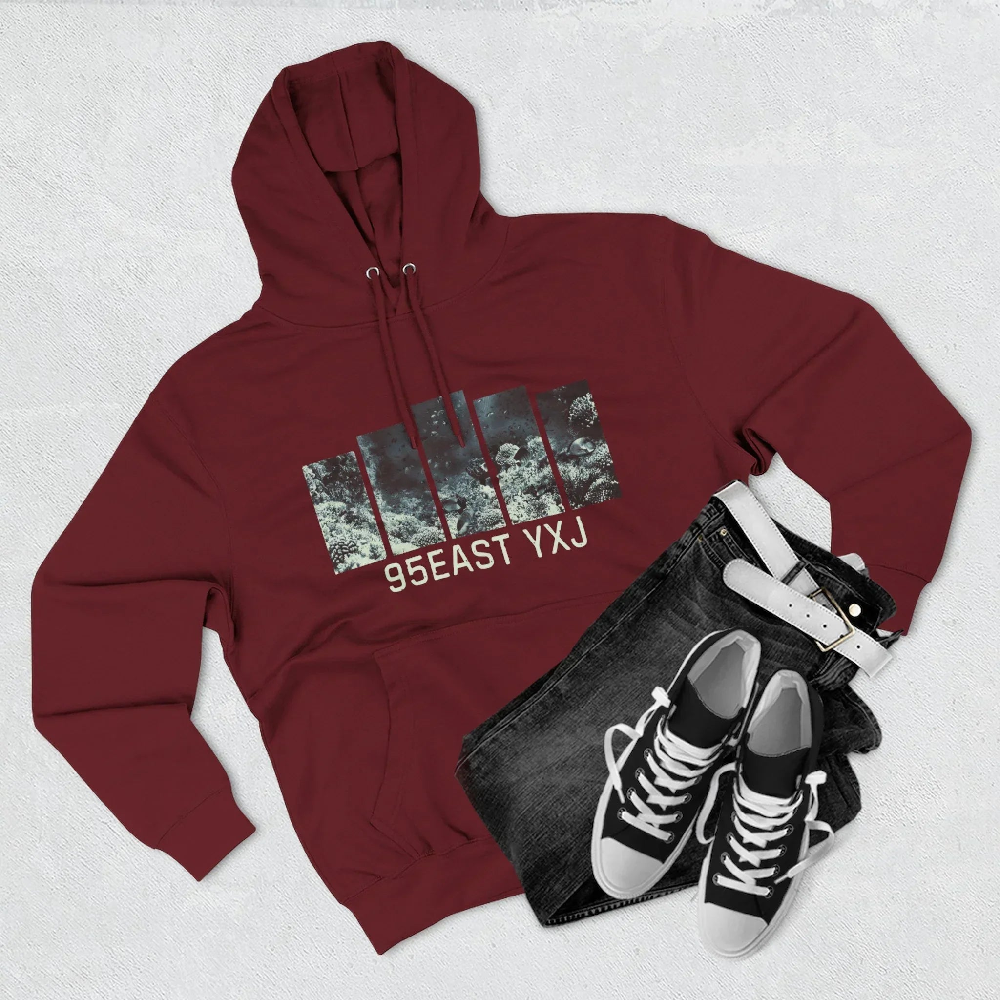 Maroon hoodie with 95EAST YXJ graphic, black jeans, white belt, and black sneakers flat lay