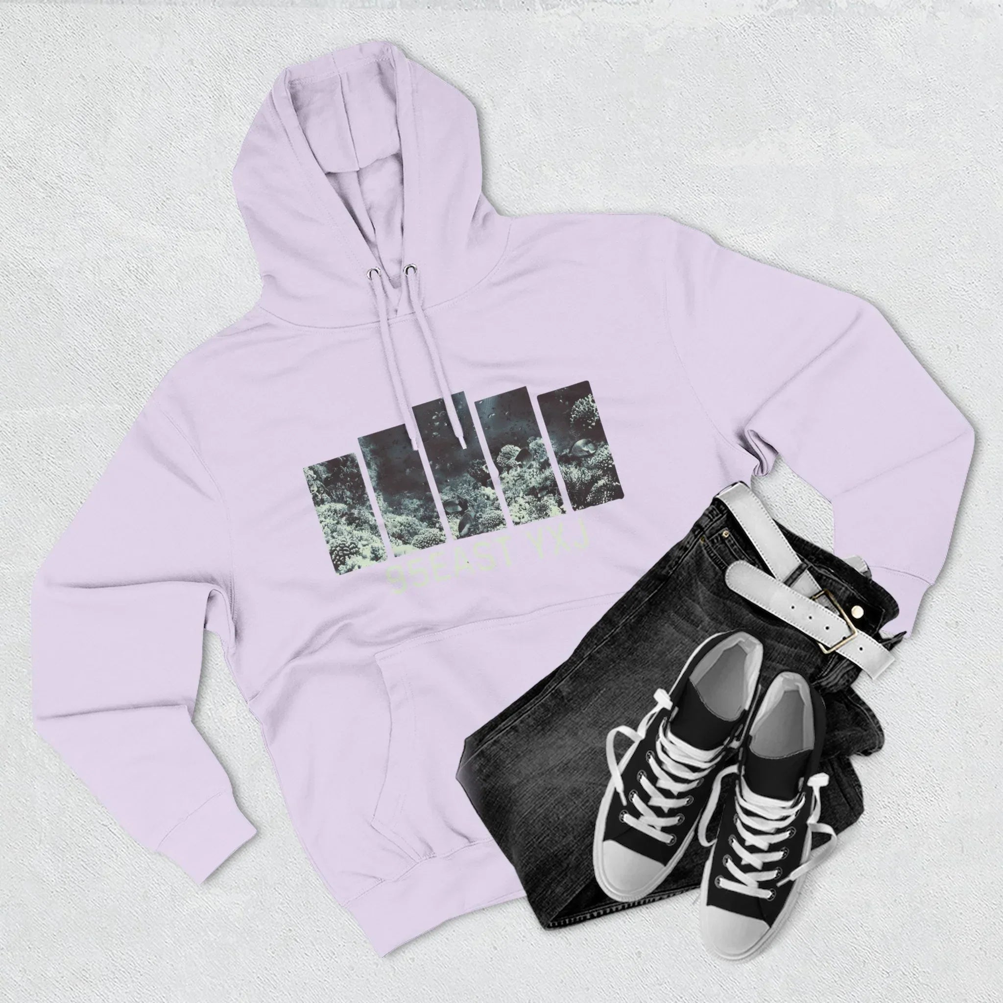 Light lavender hoodie with graphic print, black jeans with white belt, and black sneakers flat lay