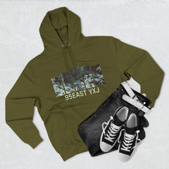 Olive green hoodie with graphic print and '95EAST YXJ' text, paired with black jeans, white belt, and black sneakers on a light background.