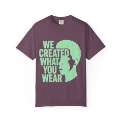 Purple t-shirt with green 'We Created What You Wear' text and silhouette graphic, lifestyle apparel design
