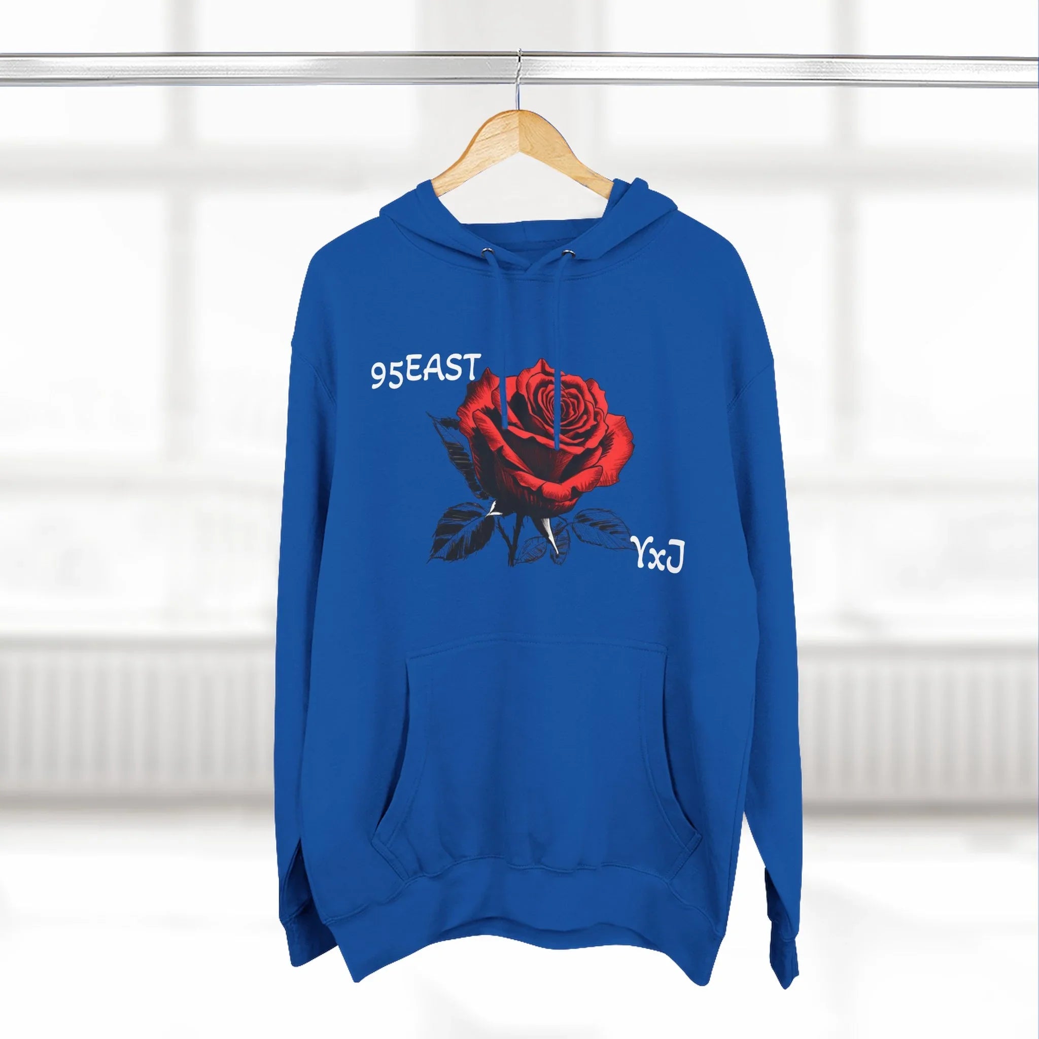 Blue hoodie with red rose graphic and '95EAST YxJ' text, hanging on wood hanger