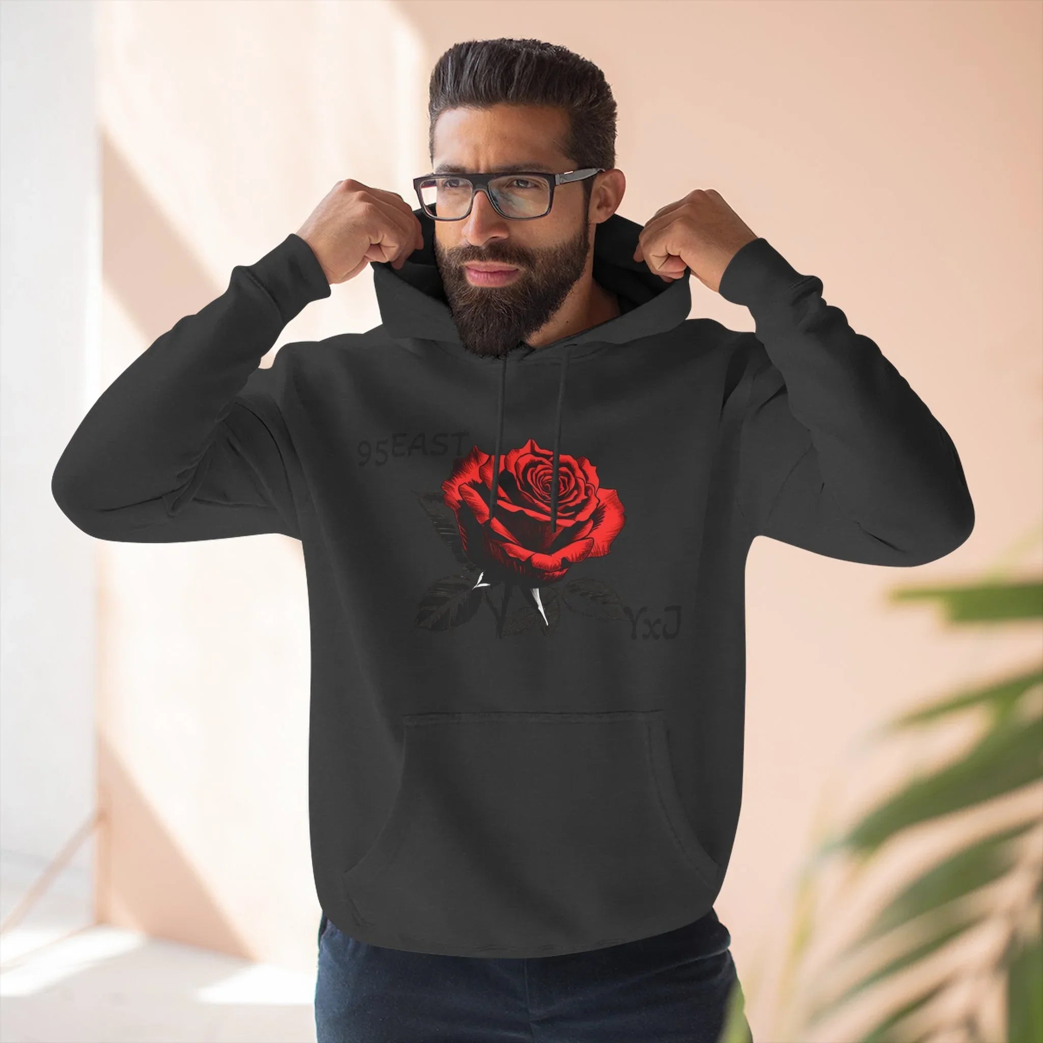 Black hoodie with red rose graphic and barcode sleeve detail, worn by man adjusting hood