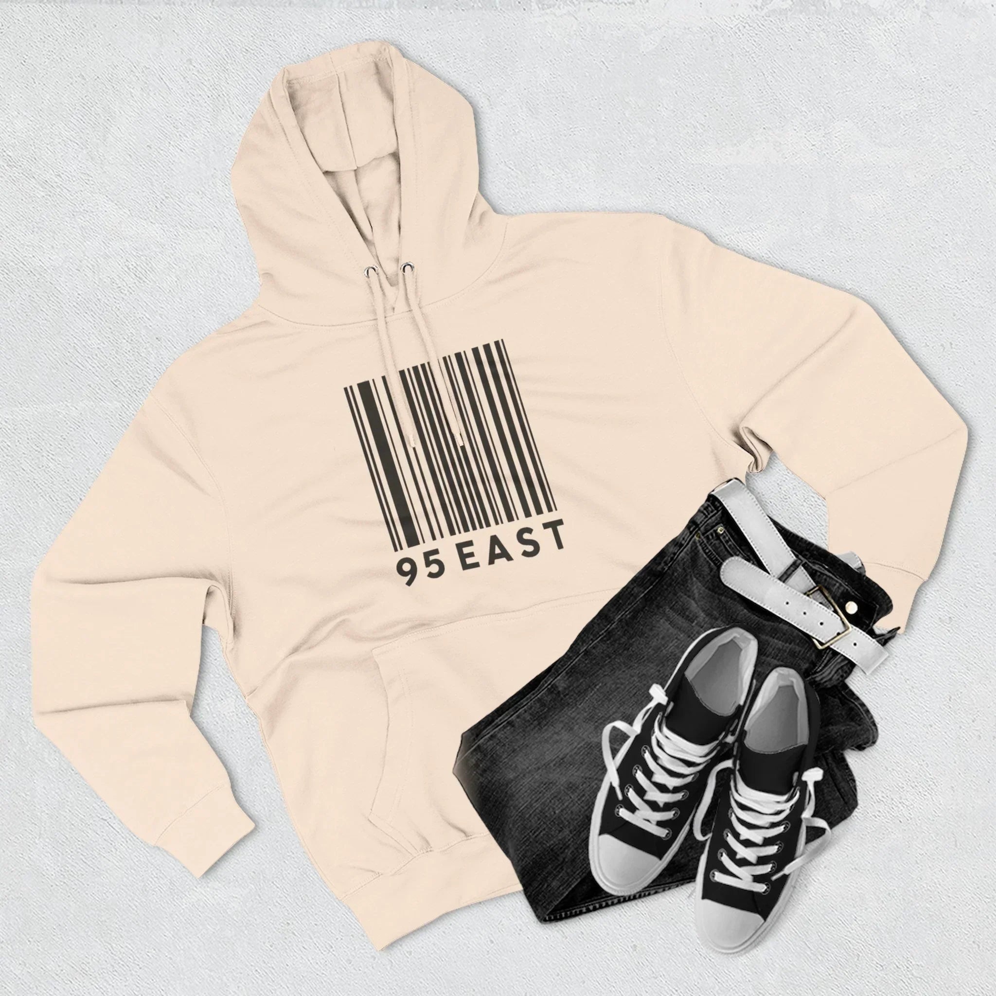 Beige hoodie with barcode design, black jeans, and sneakers styled together