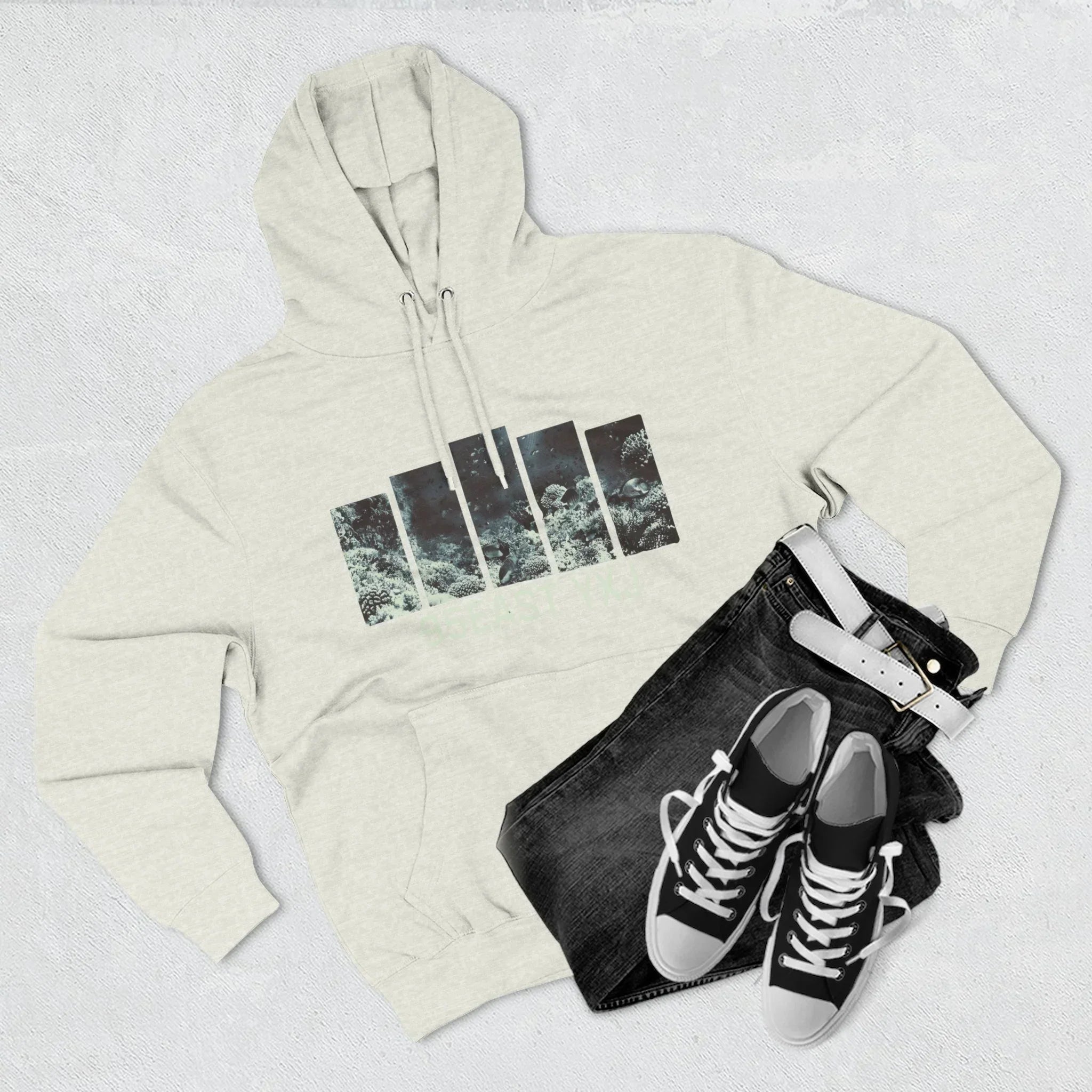 Flat lay of light gray graphic hoodie with nature print, black jeans, white belt, and sneakers.