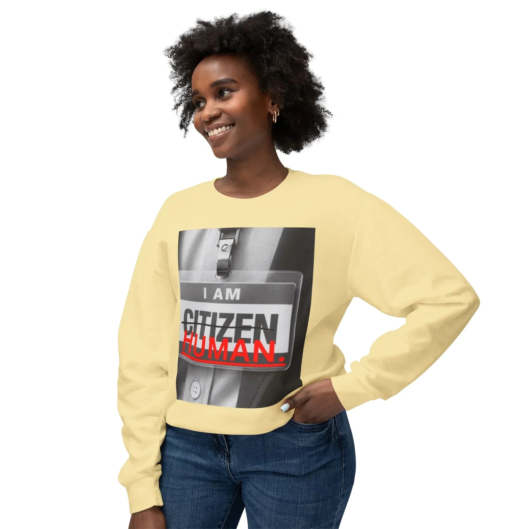 Smiling woman in yellow sweatshirt with 'I am human' graphic and jeans on white background
