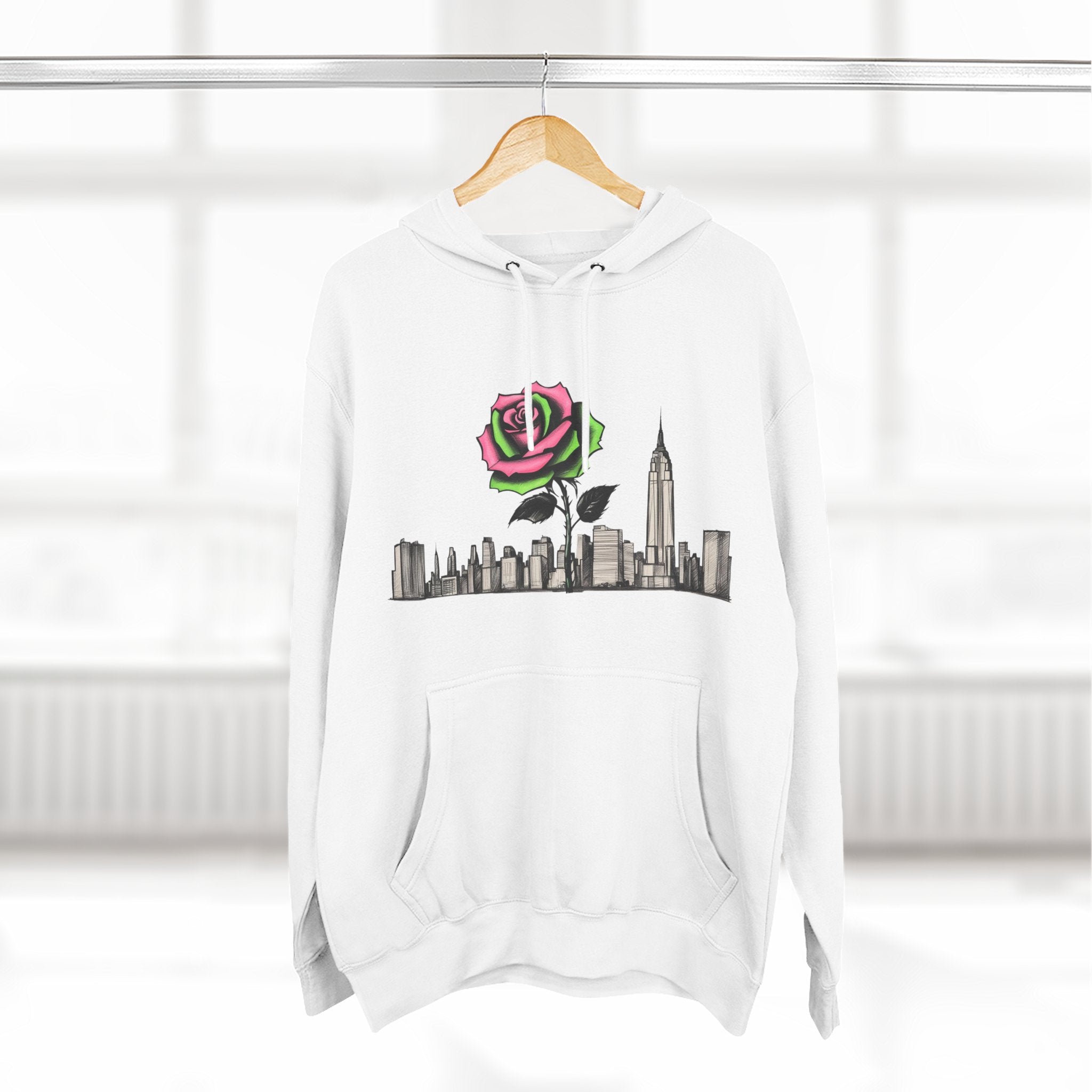 White hoodie with pink rose and NYC skyline graphic, hanging on wood hanger