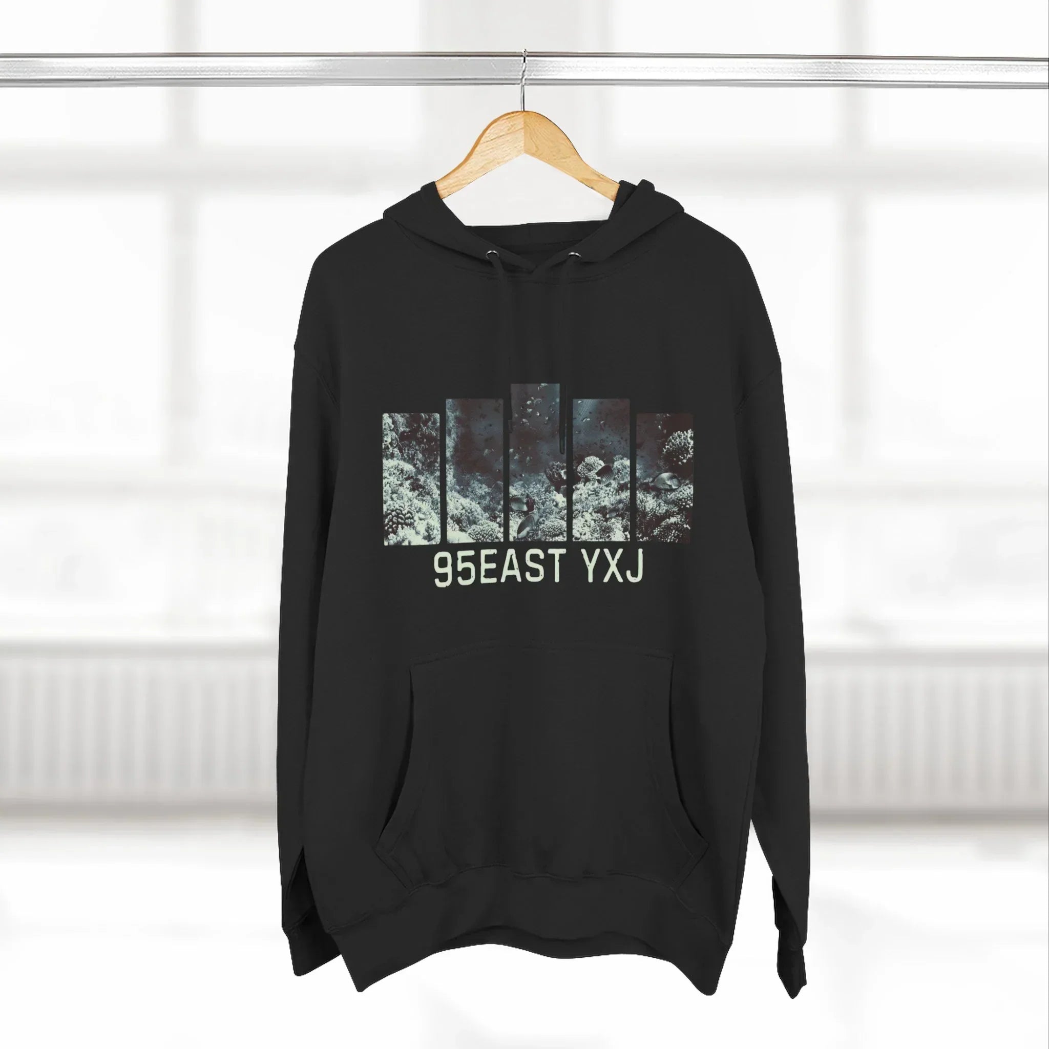 Black hoodie with graphic bars and text '95EAST YXJ' hanging on wooden hanger