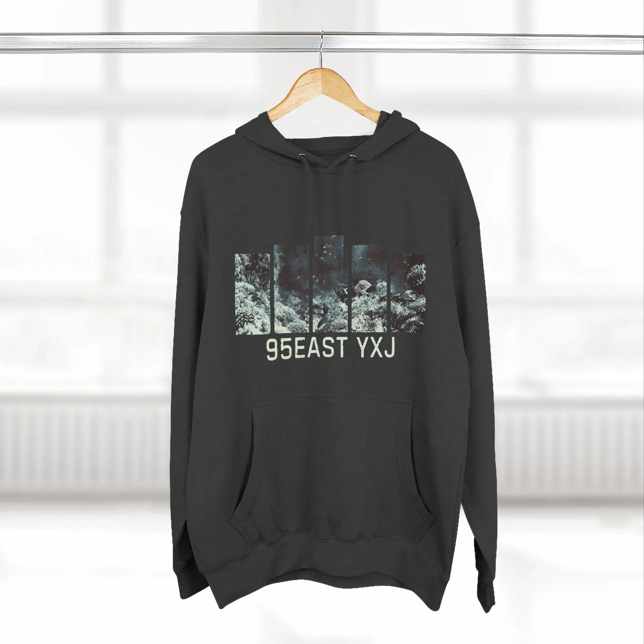 Black hoodie with abstract nature graphic and 95EAST YXJ text, hanging on a wooden hanger