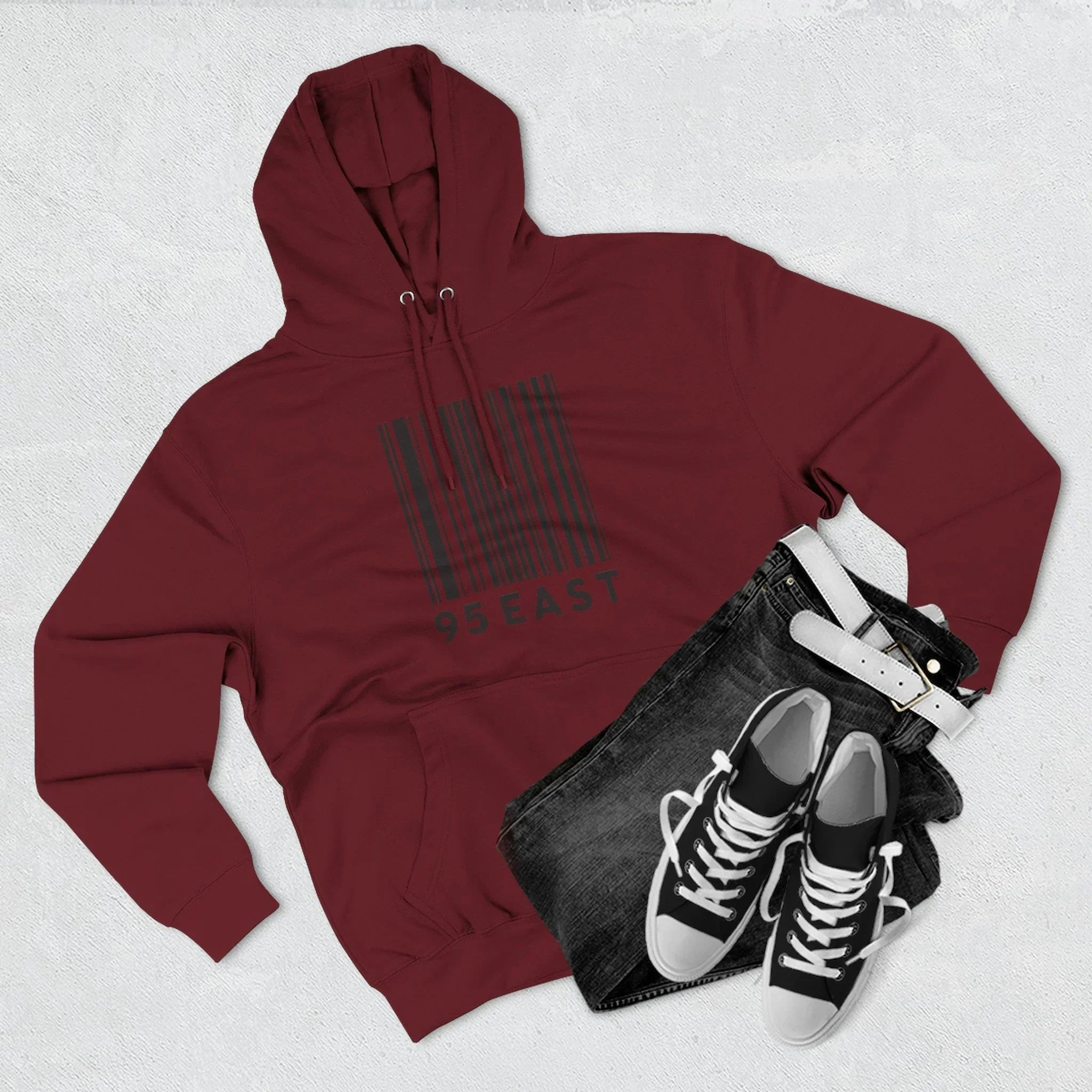 Maroon hoodie with barcode 95 EAST graphic, paired with black jeans and classic high-top sneakers for casual streetwear style.