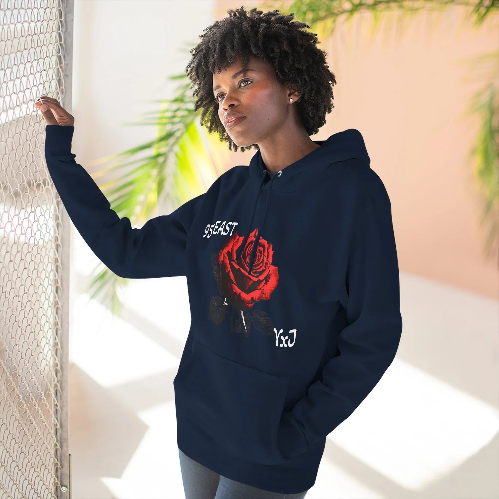 Black hoodie with red rose graphic and barcode sleeve detail, worn by woman near mesh fence