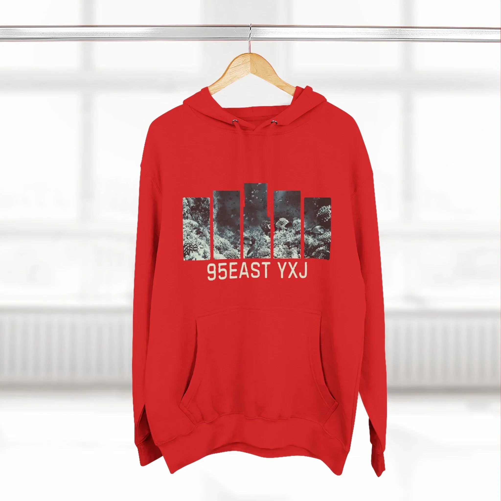 Red hoodie with abstract graphic bars and '95EAST YXJ' text, hanging on a wooden hanger