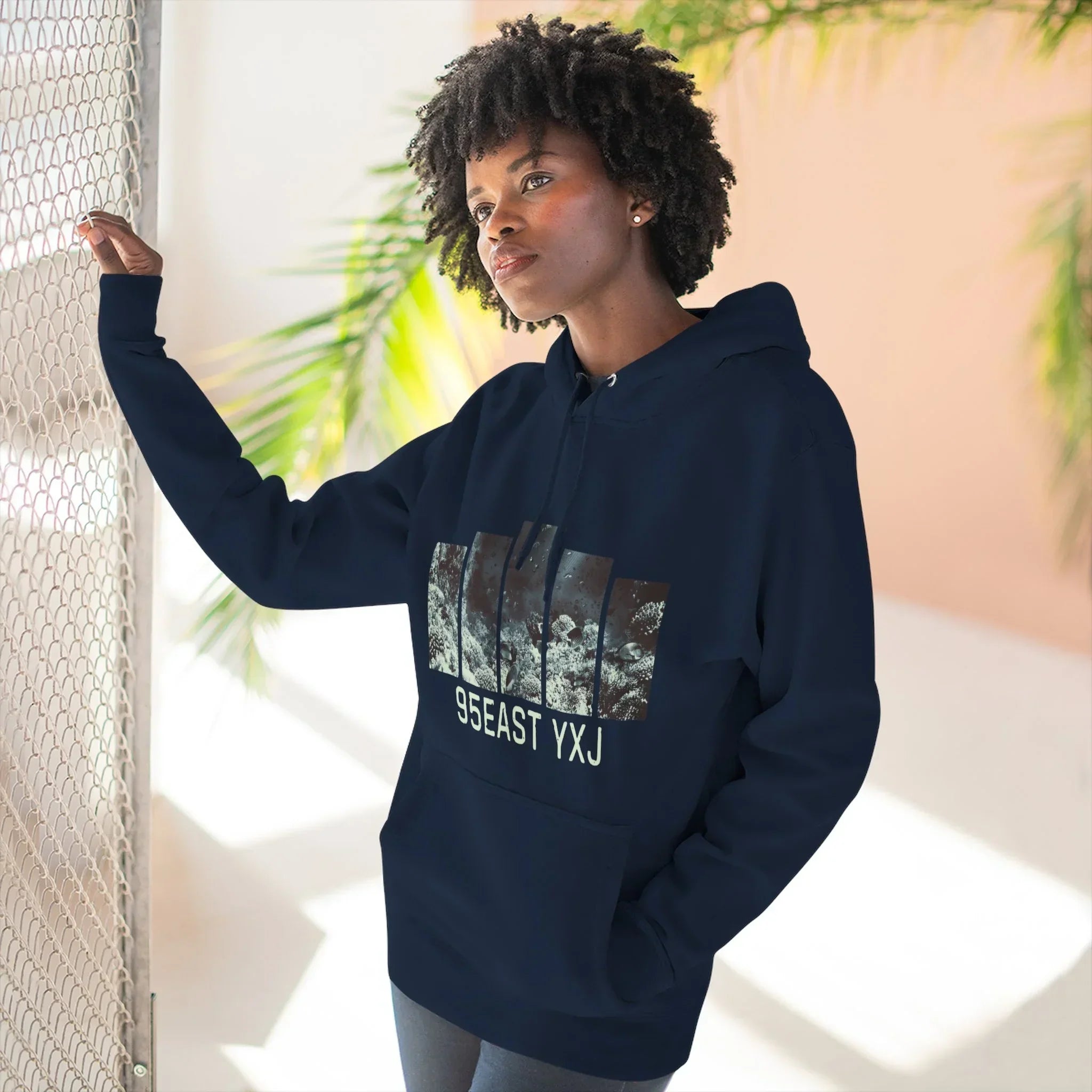 Woman in navy hoodie with graphic print and '95EAST YXJ' text, standing by fence outdoors