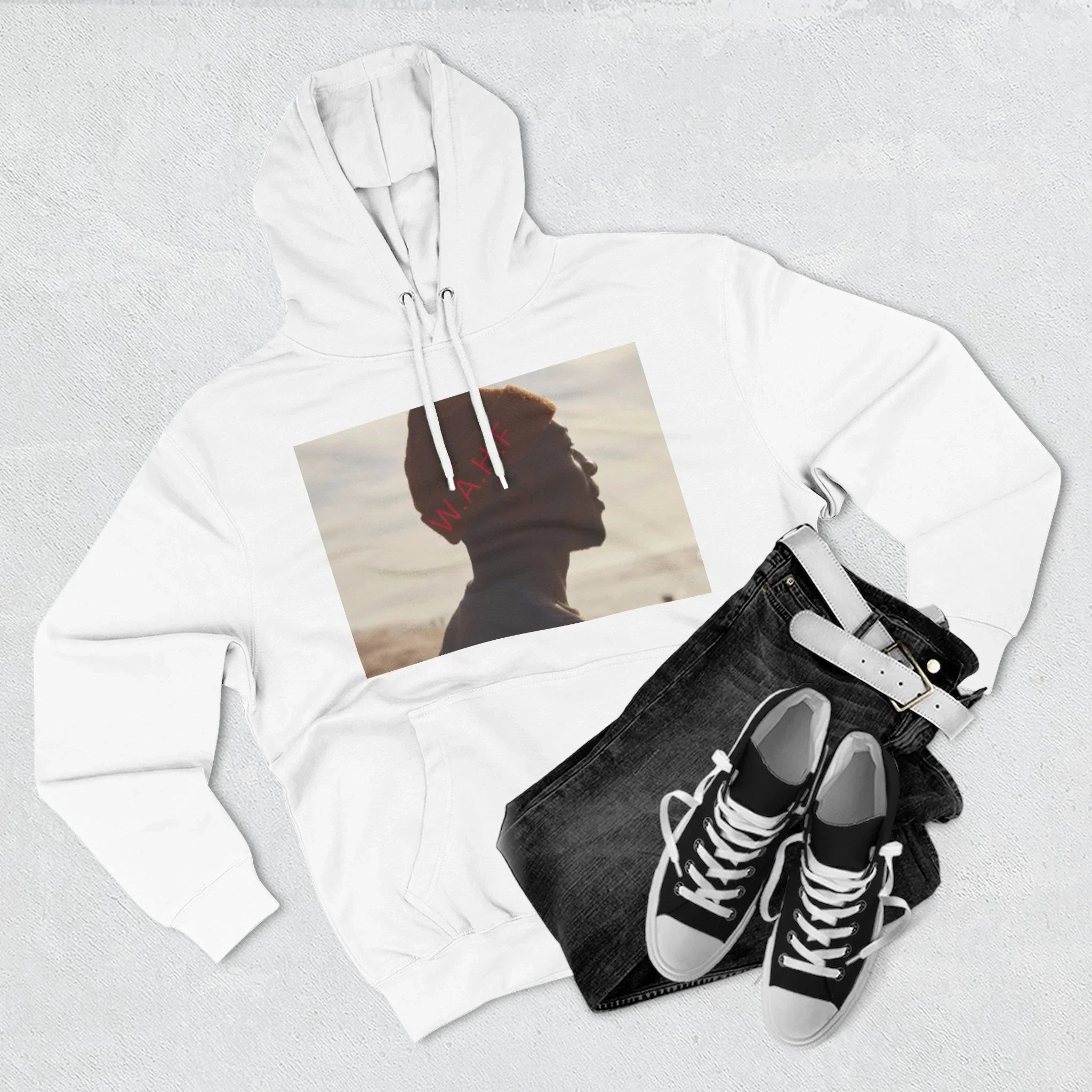 Flat lay of white hoodie with graphic print, black jeans, black sneakers, and a white belt