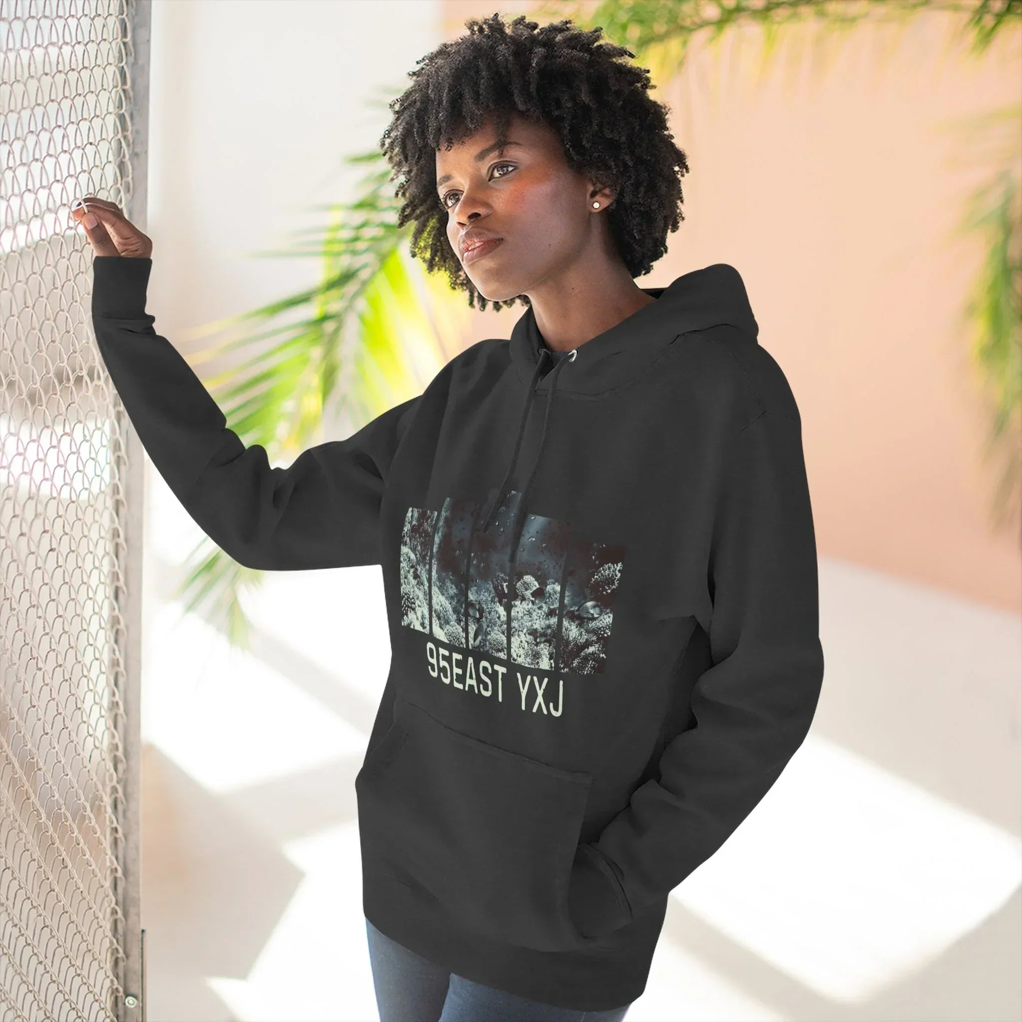 Woman in black hoodie with forest graphic and '95EAST YXJ' text, standing outdoors