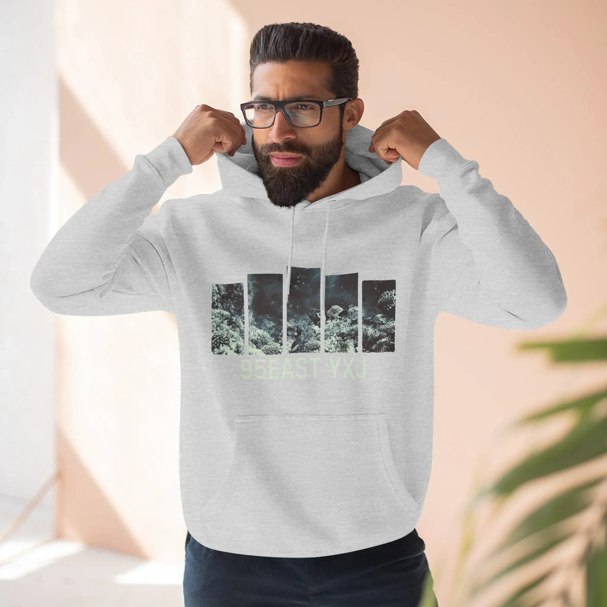 Man wearing light grey hoodie with graphic bars and '95EAST YXJ' text, standing indoors.