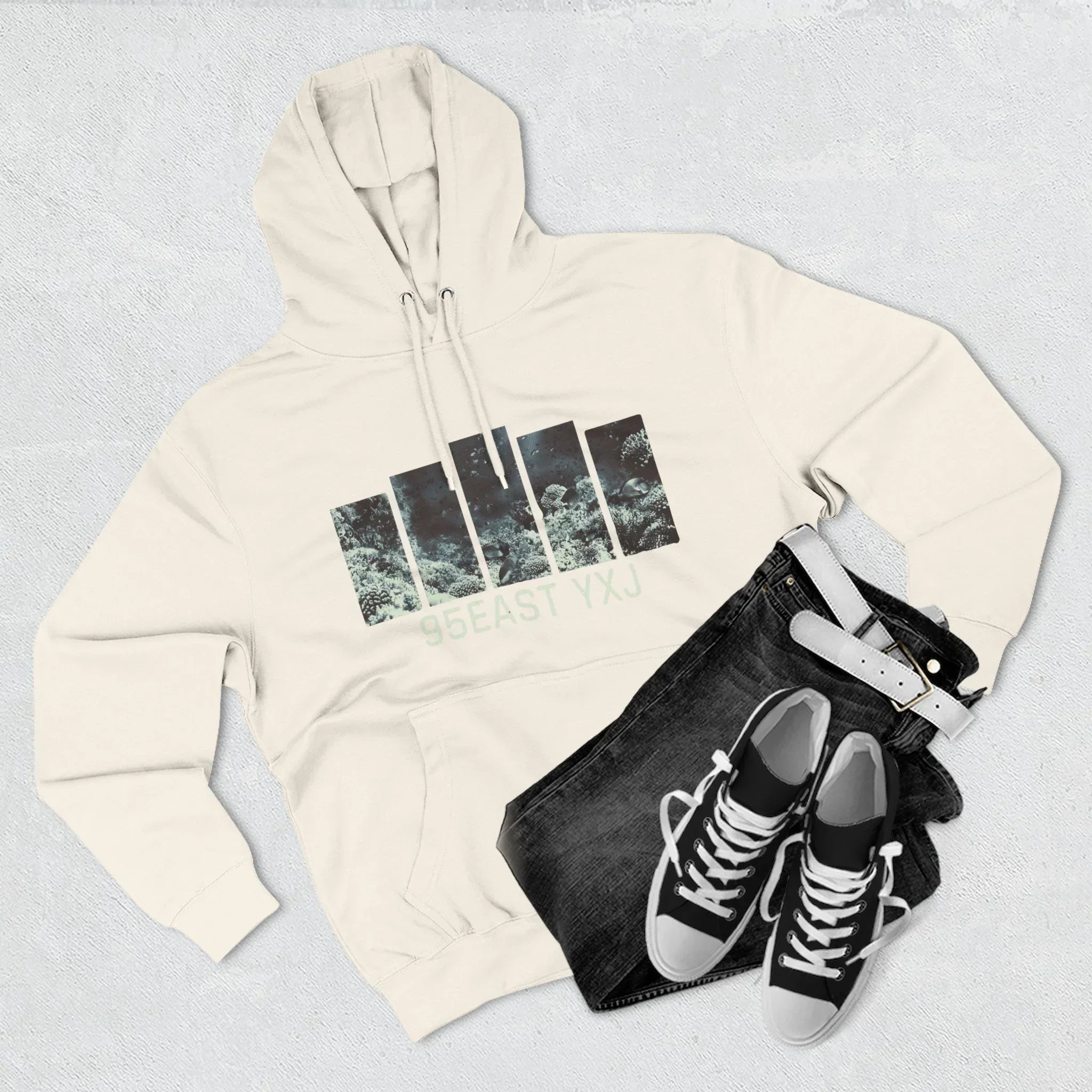 Cream hoodie with graphic print, black jeans, white belt, and black sneakers on a light surface