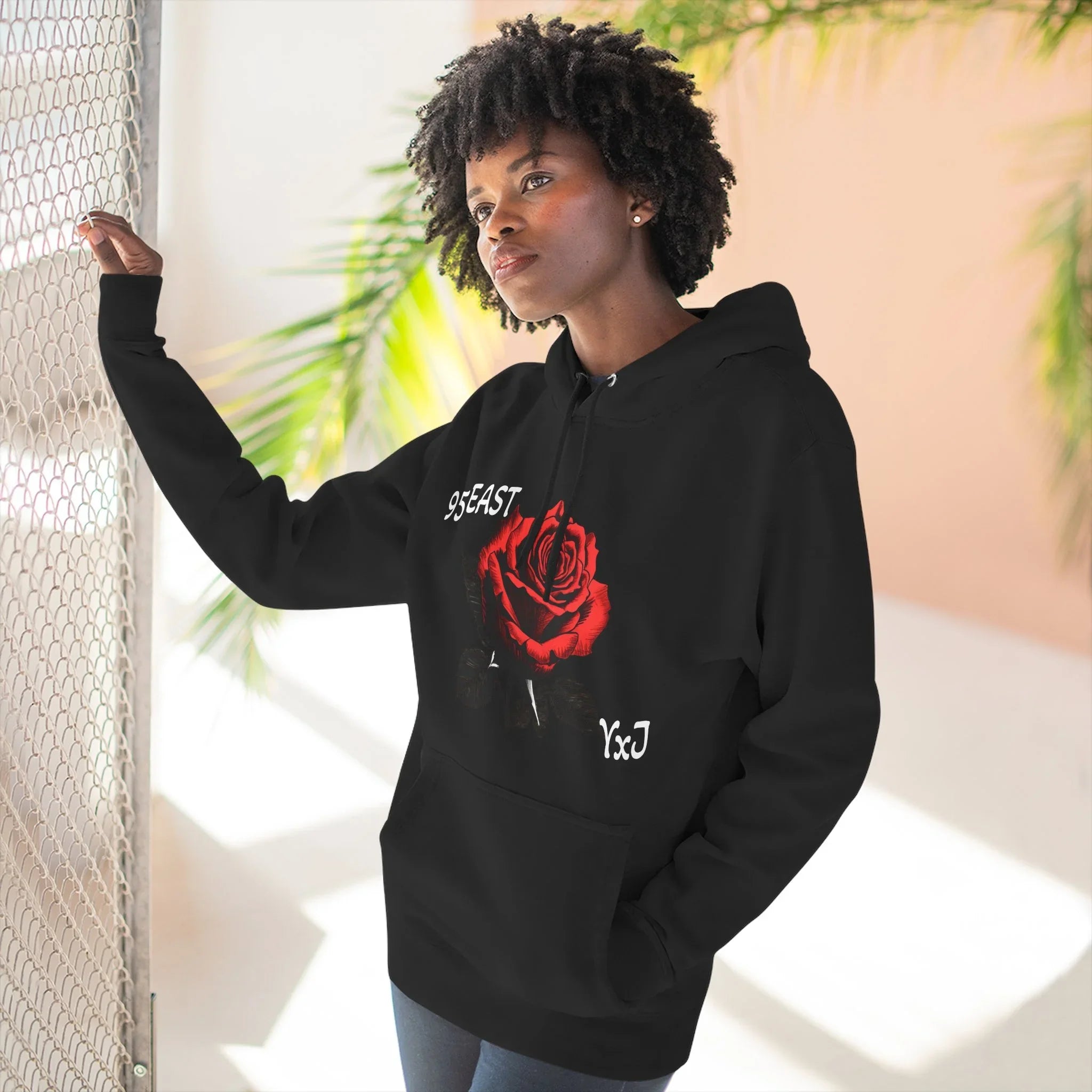 Black hoodie with red rose graphic and barcode sleeve detail, worn by woman near chain-link fence