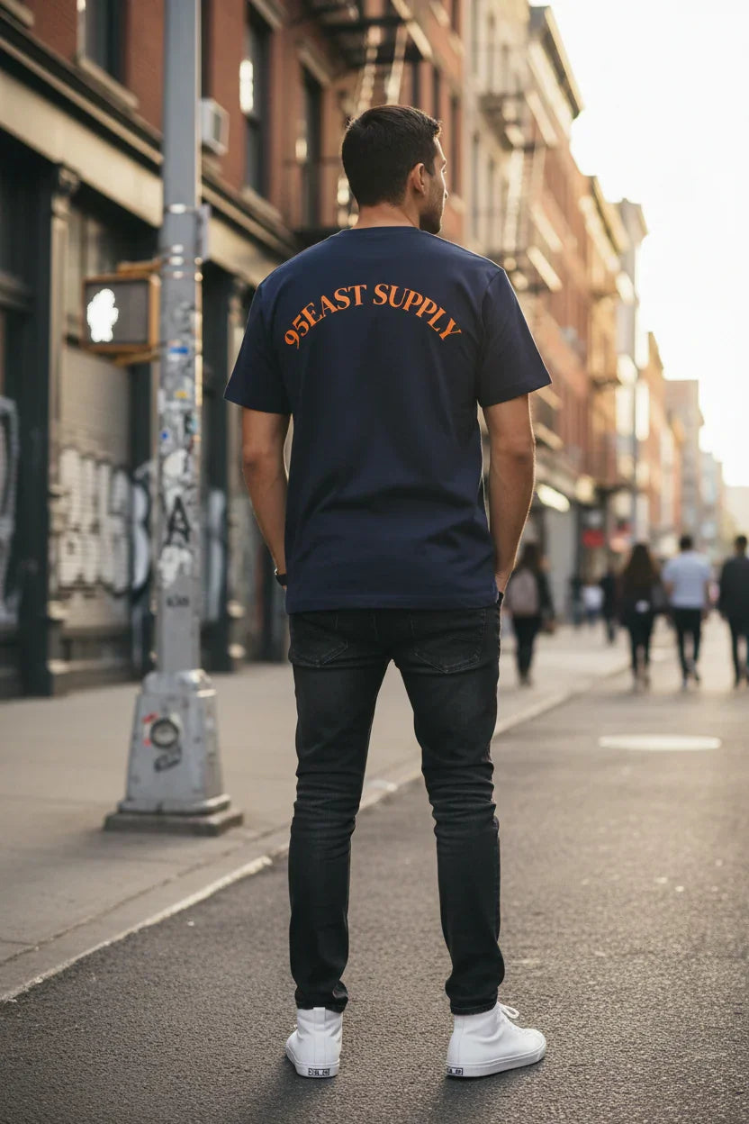 Man wearing navy 95EAST SUPPLY t-shirt, black jeans, white sneakers on urban street