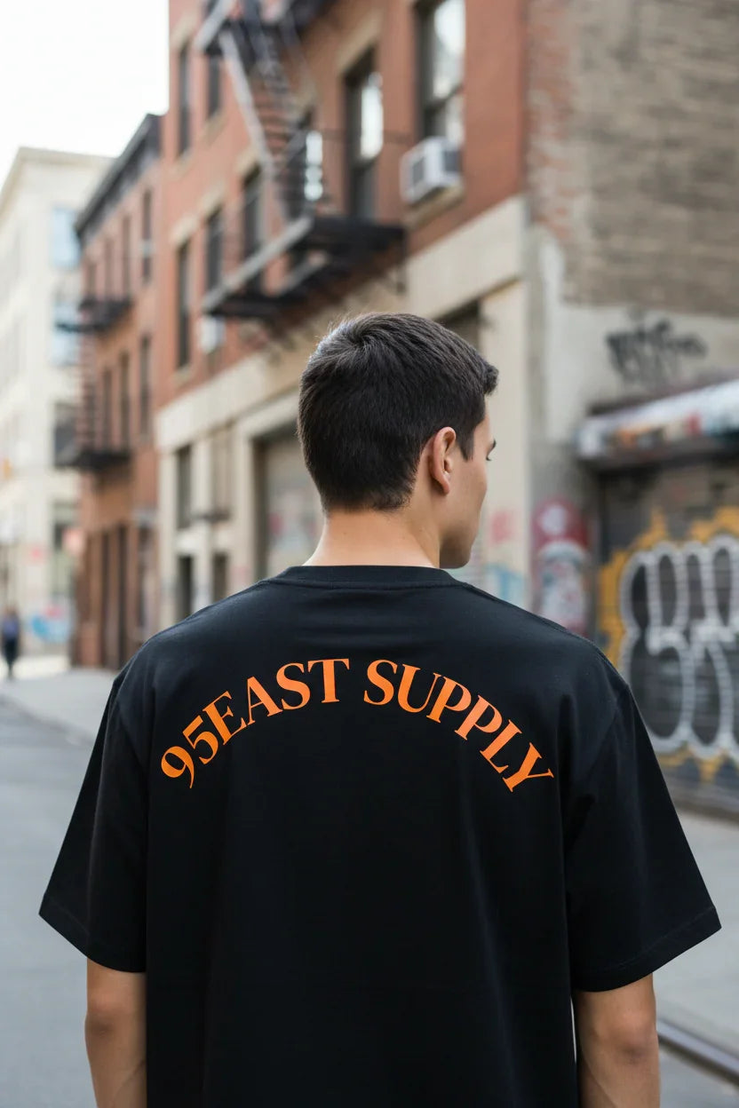 Man wearing black 95EAST SUPPLY t-shirt on urban street with graffiti