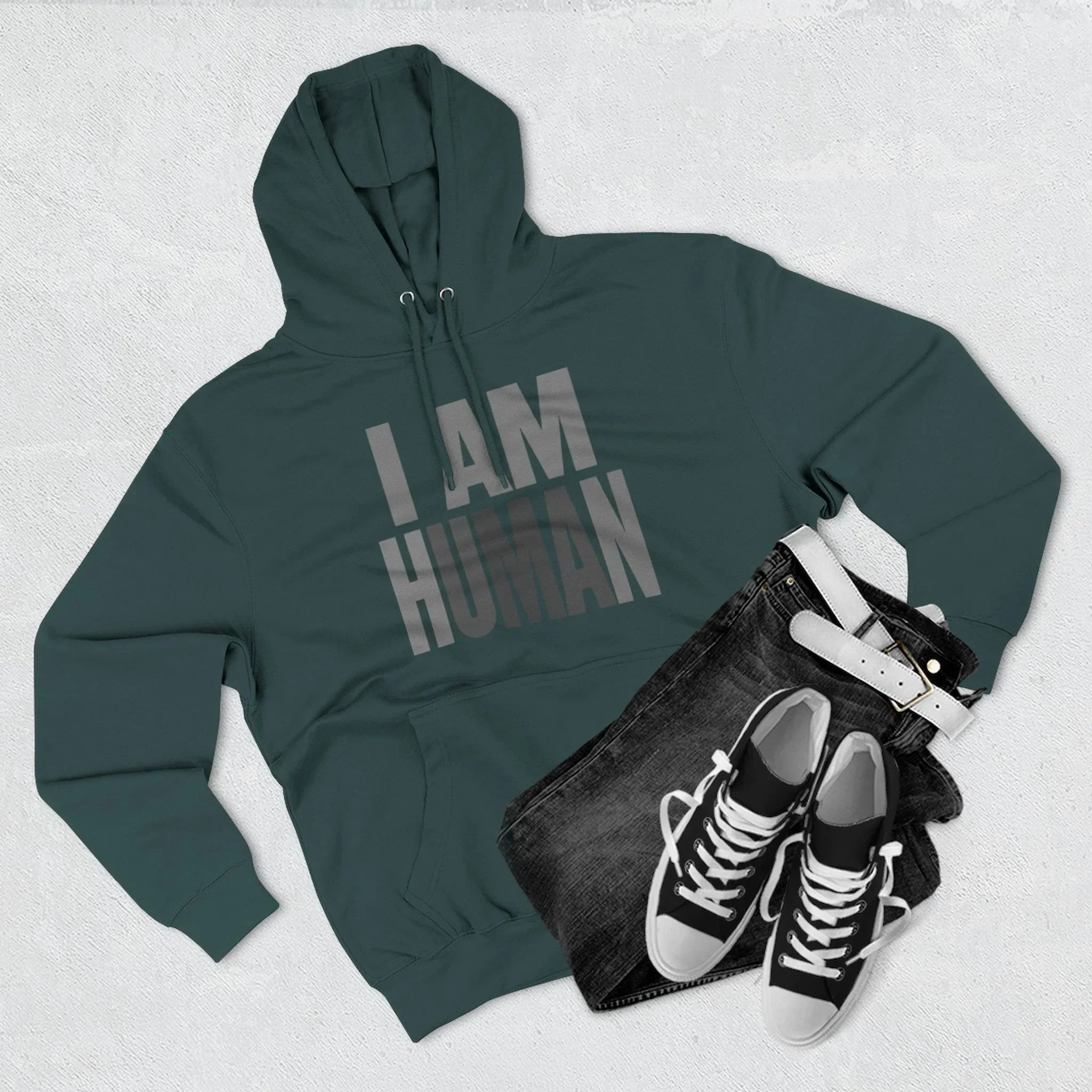 Green I AM HUMAN hoodie with black jeans, black sneakers, and white belt on light background