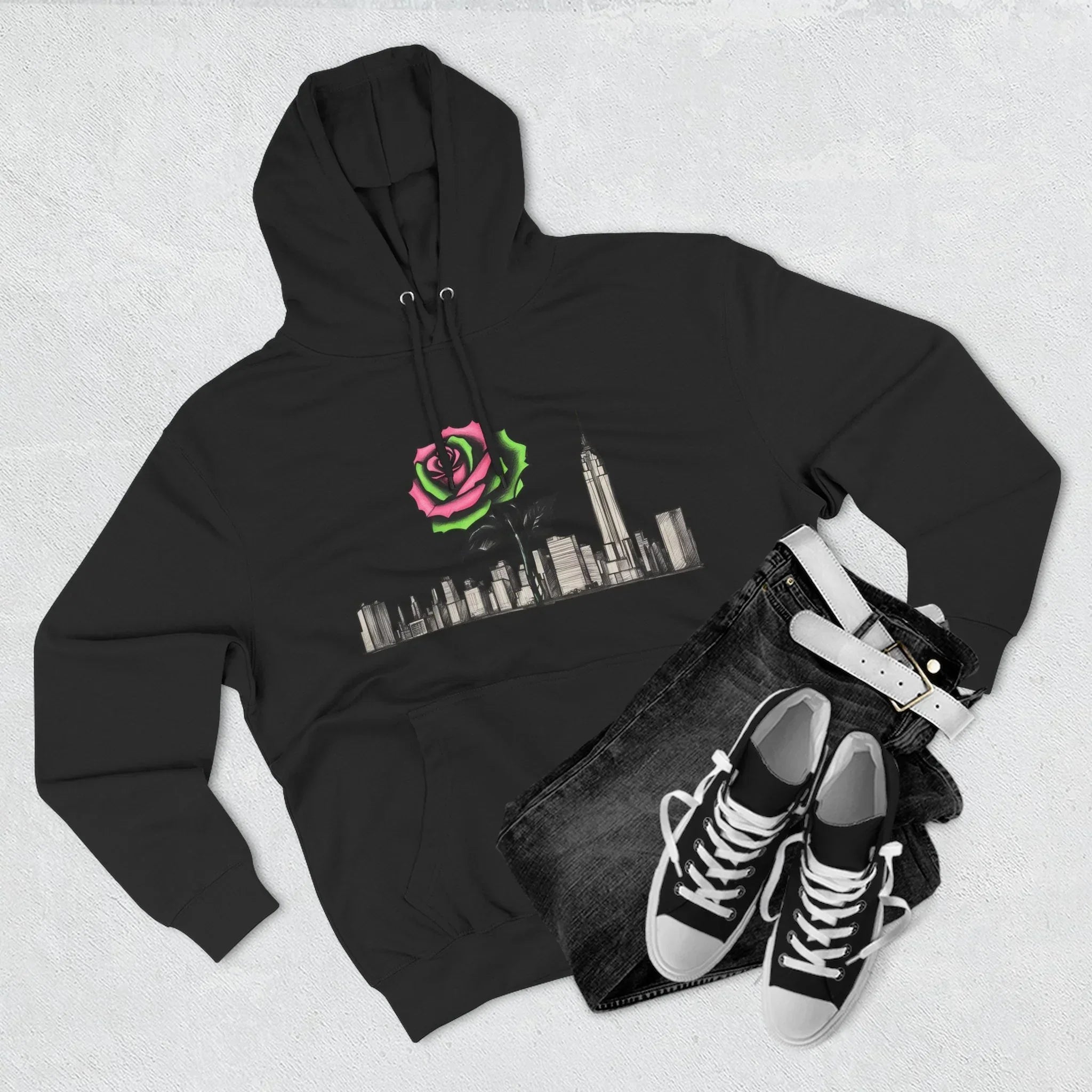 Black hoodie with a neon rose and city skyline graphic, paired with jeans, belt, and sneakers.