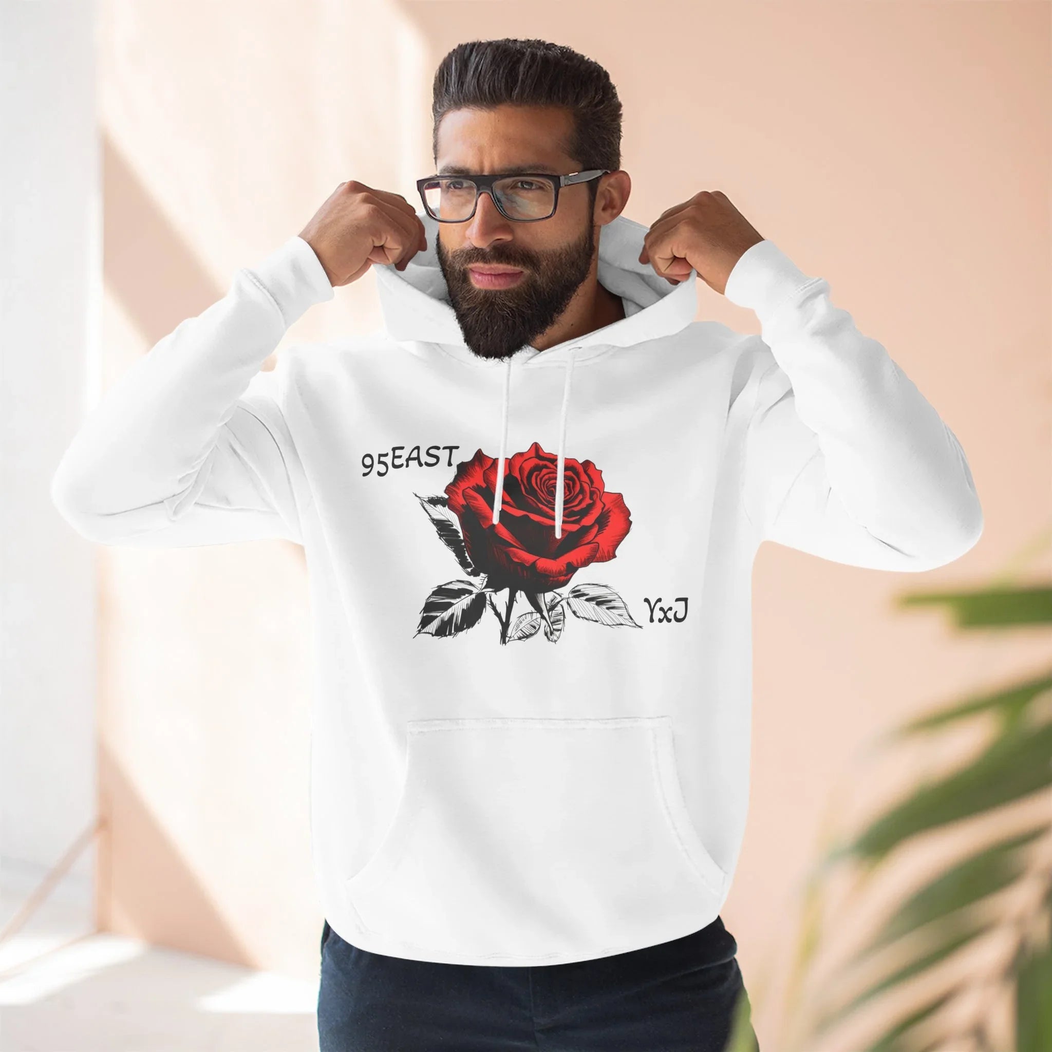 White hoodie with red rose graphic and 95EAST YxJ text, worn by man adjusting hood
