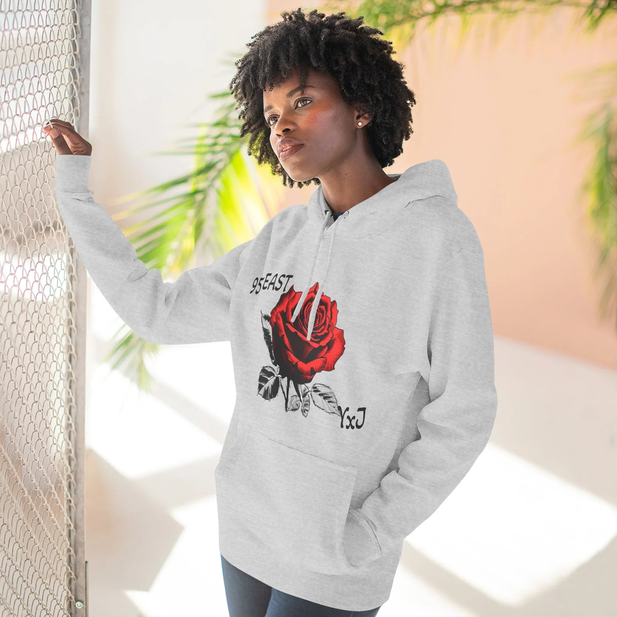 Gray hoodie with red rose graphic and YxJ text, worn by woman near mesh fence and palm leaves