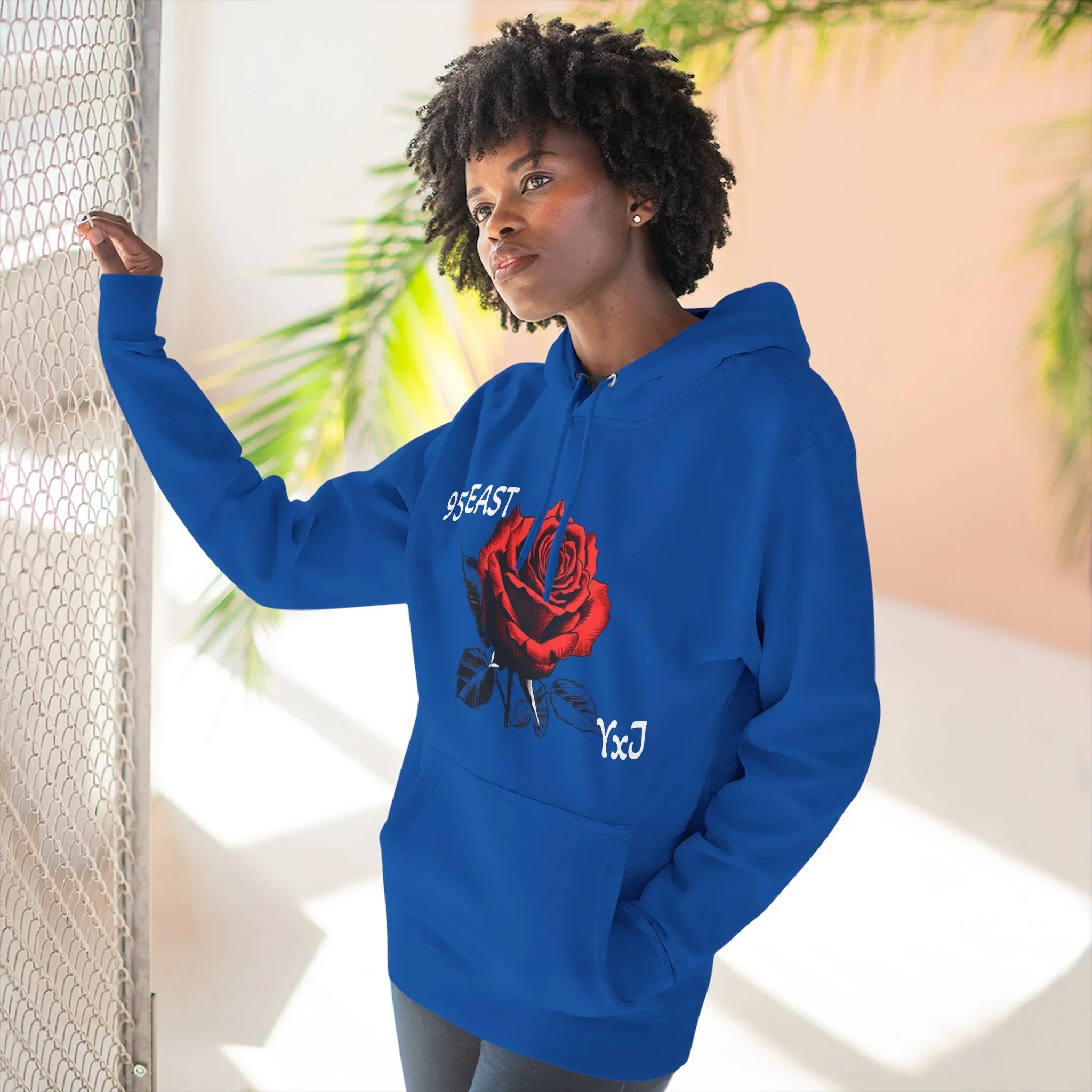 Blue hoodie with red rose graphic and YxJ text, worn by woman near chain-link fence
