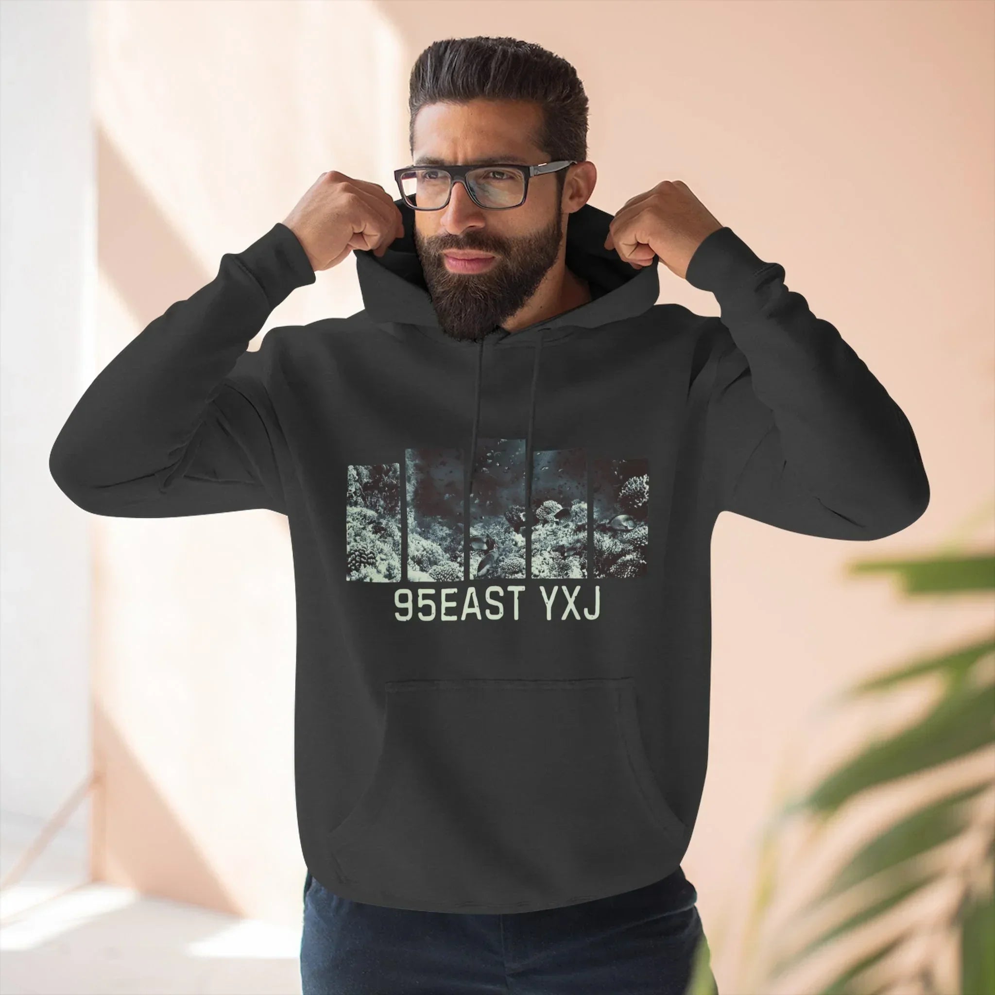 Man adjusting black hoodie with 95EAST YXJ text and graphic, modern casual fashion