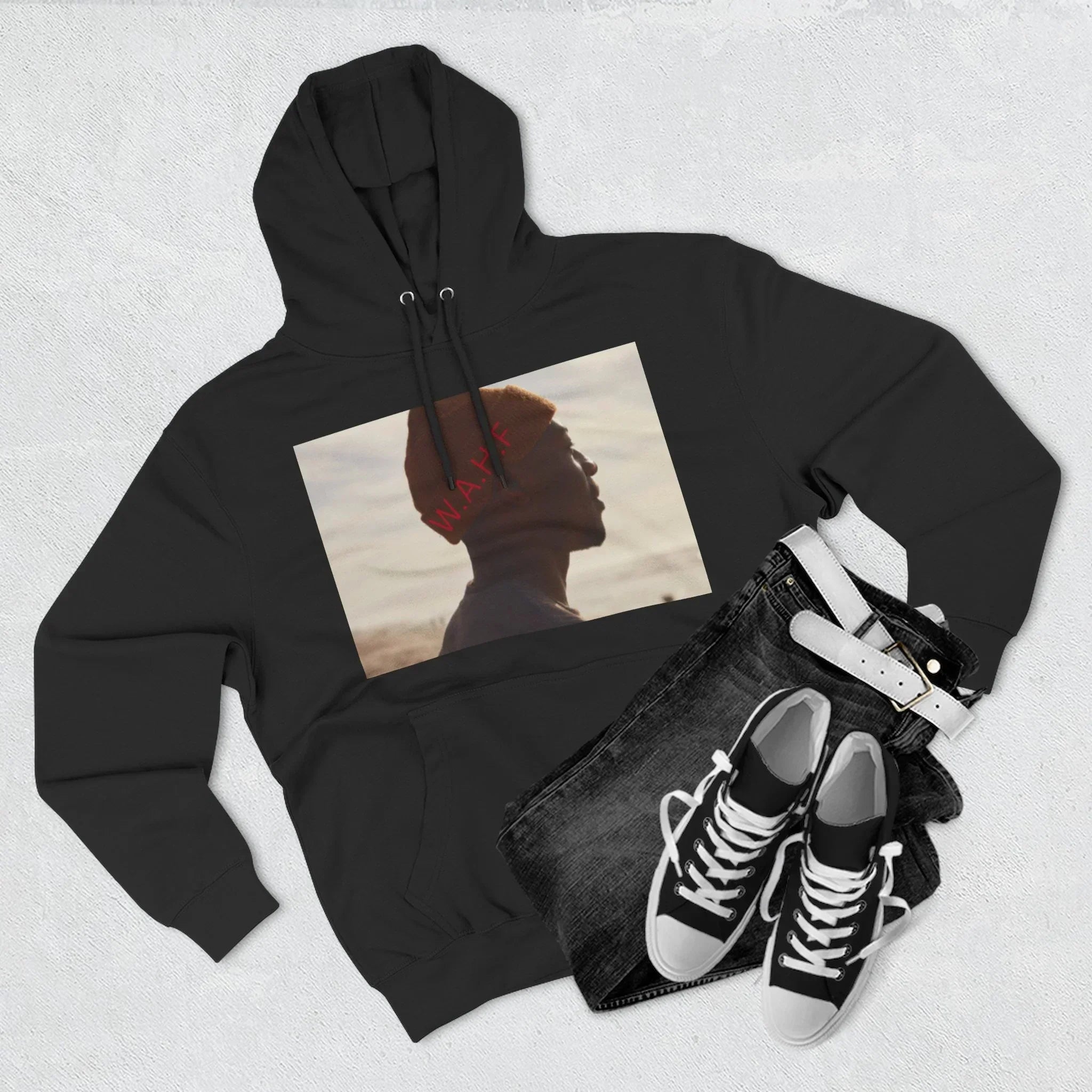 Black hoodie with artistic portrait print, paired with black jeans, white belt, and sneakers.