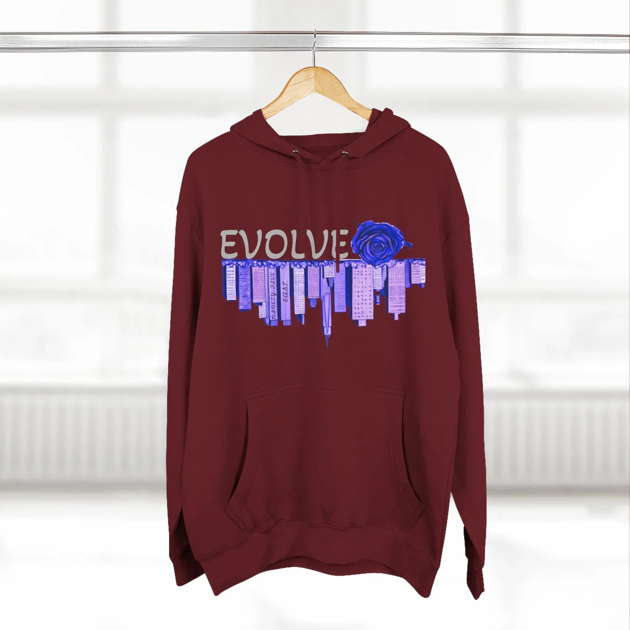 Maroon hoodie with EVOLVE text, blue rose, and city skyline graphic, hanging on hanger