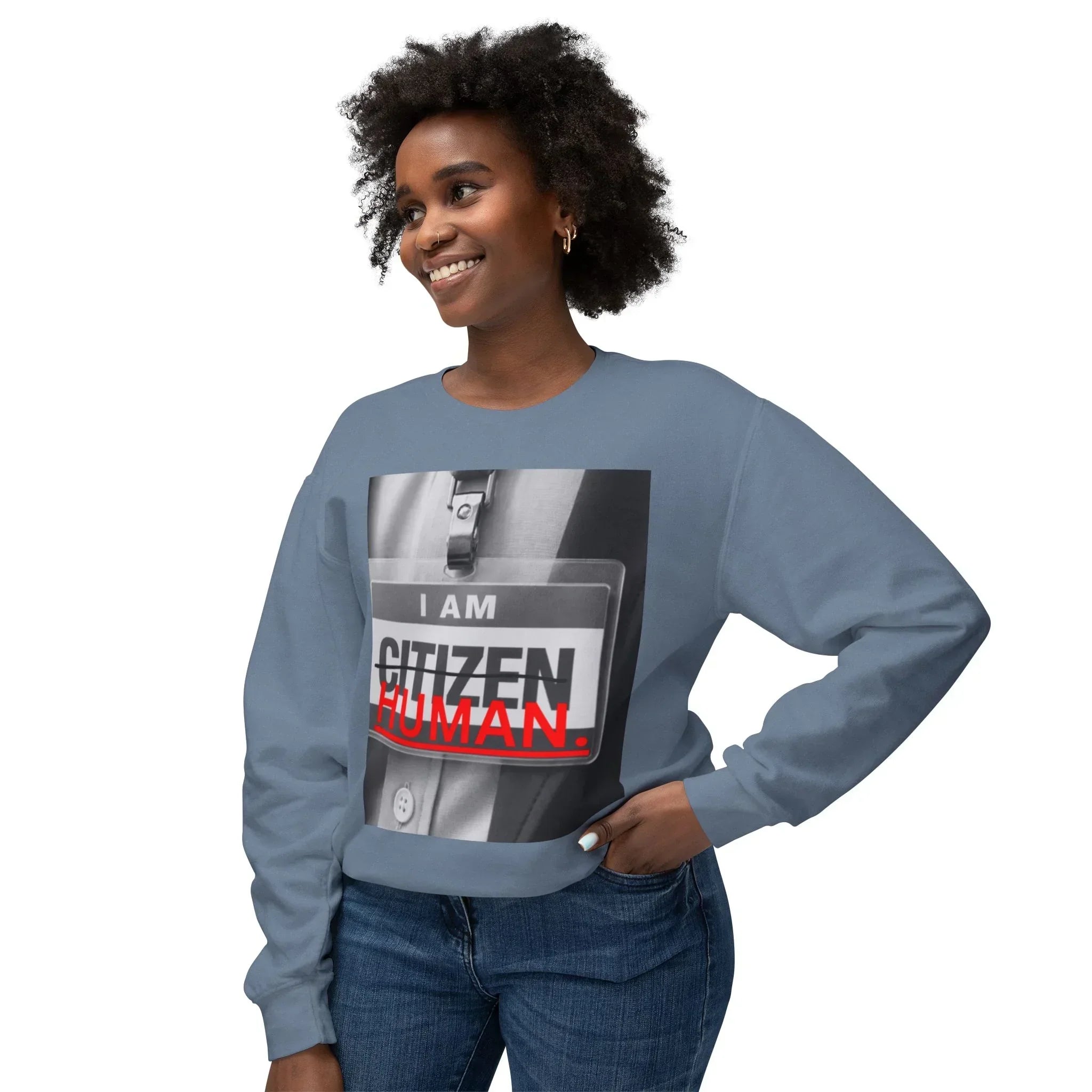 Smiling woman in blue sweatshirt with 'I AM HUMAN' graphic and jeans, casual streetwear style.