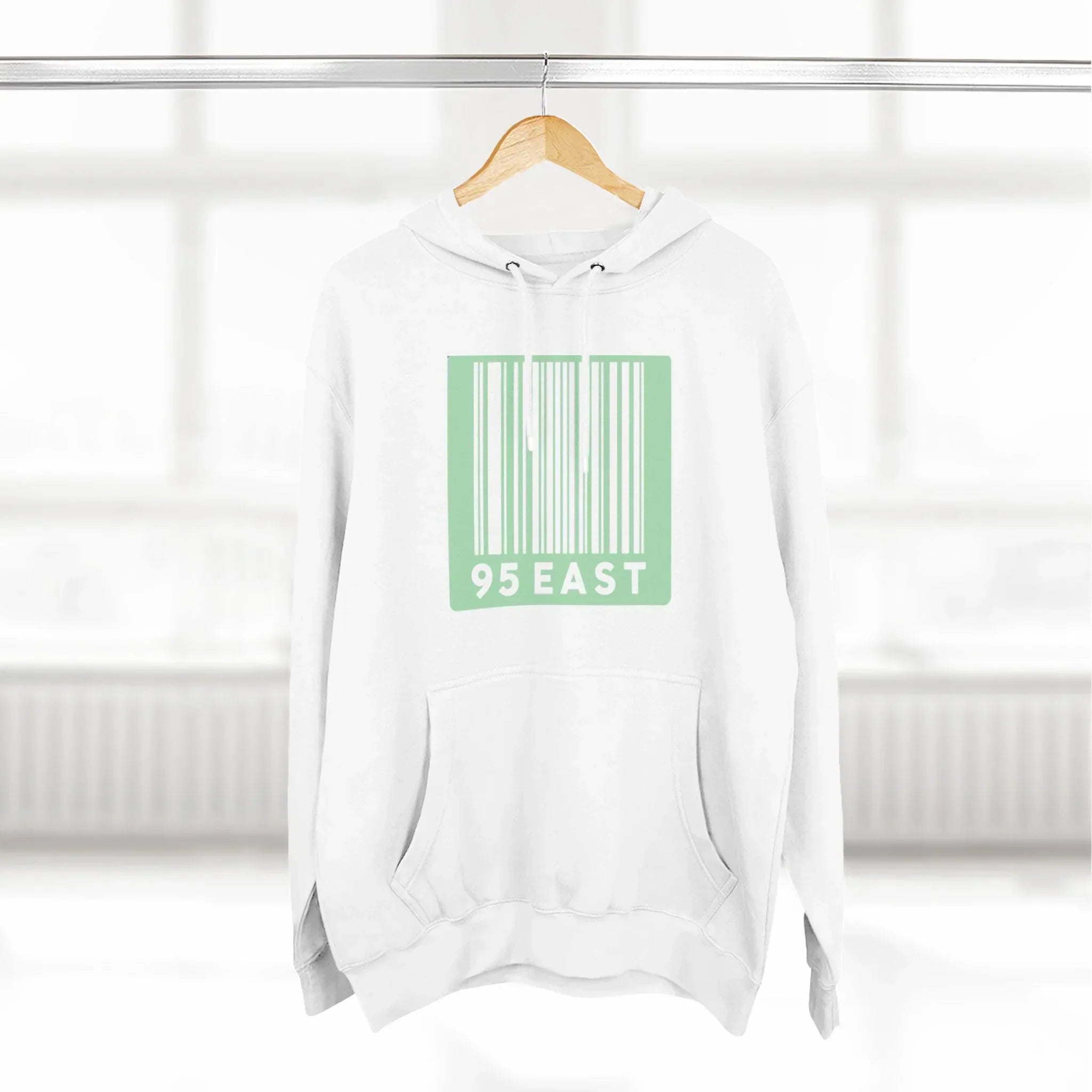White hoodie with green barcode design and 95 EAST text, hanging on wooden hanger