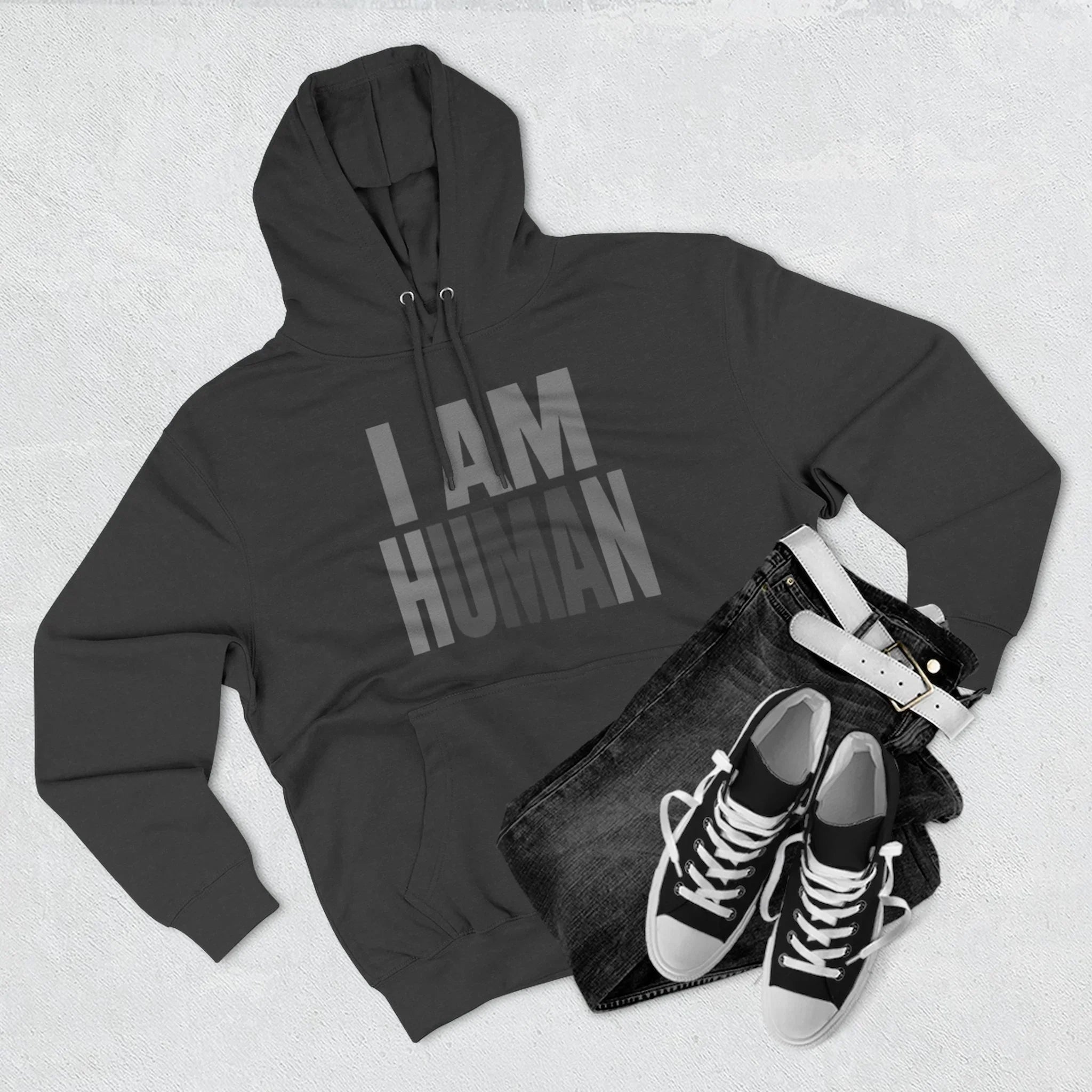 Black I AM HUMAN hoodie paired with dark jeans, white belt, and black sneakers on flat surface