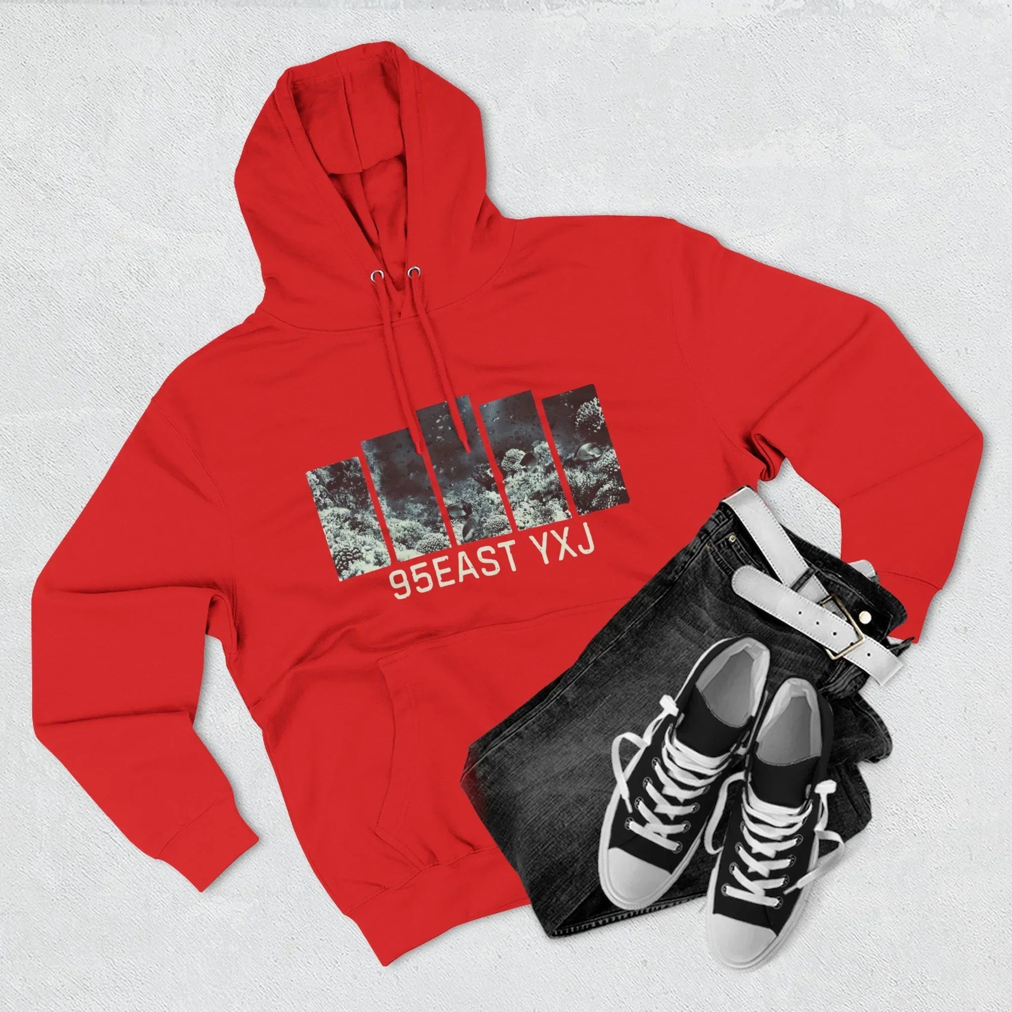 Red hoodie with abstract graphic and '95EAST YXJ' text, paired with black jeans, belt, and sneakers