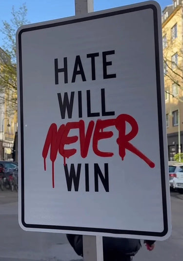 Street sign with 'HATE WILL NEVER WIN' message, red graffiti-style lettering, urban background